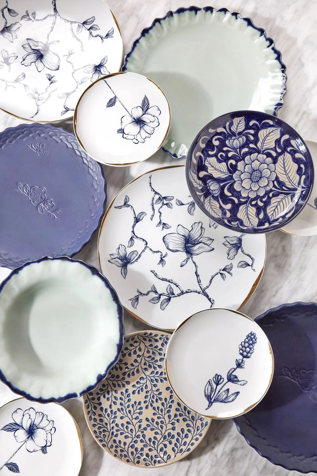 A collection of decorative porcelain bowls with white and blue floral and botanical designs, some with gold rims, arranged on a light marble surface.