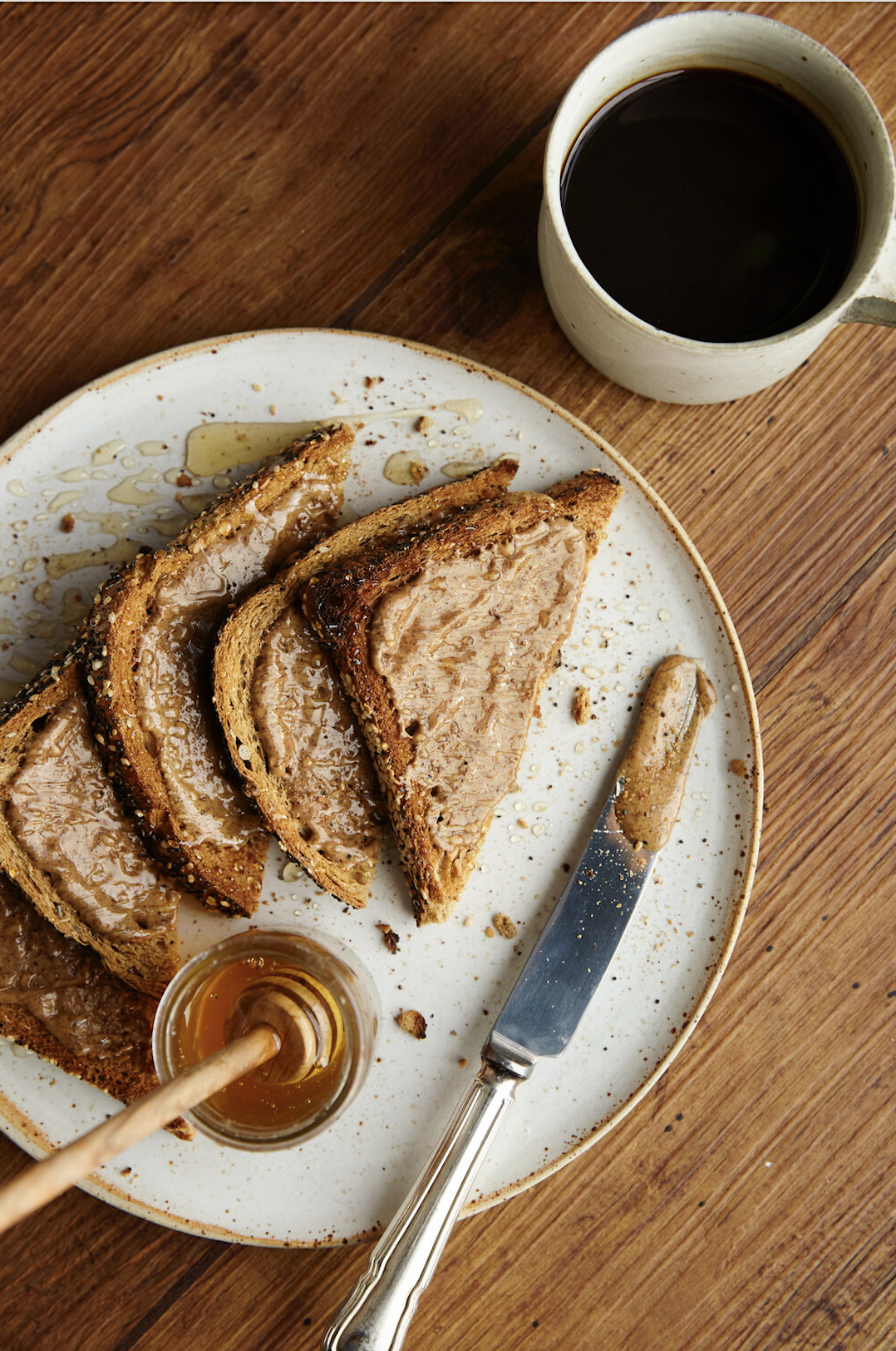 Sliced foie gras on a white plate with honey and a knife, alongside a cup of black coffee on a wooden table.