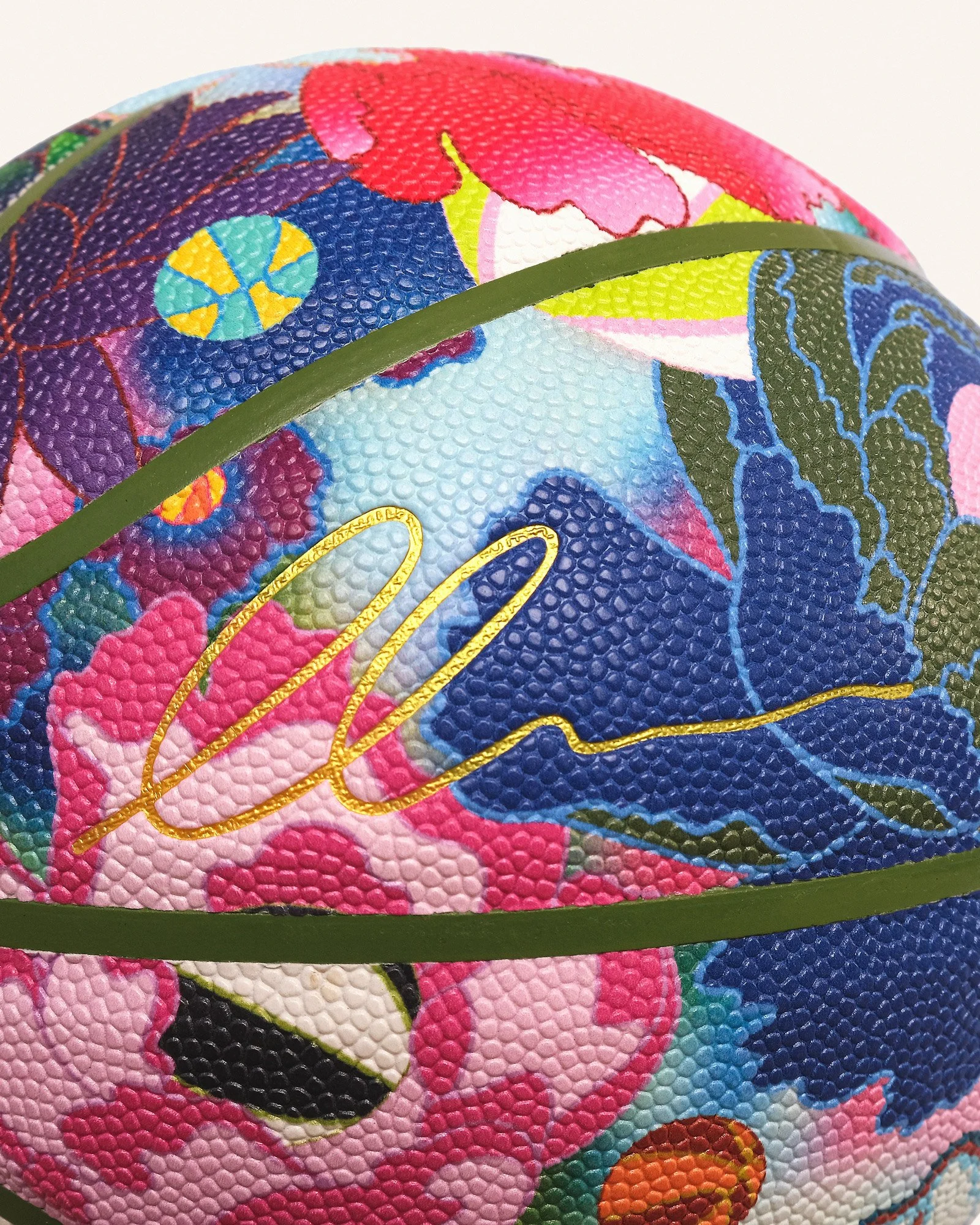 Close-up detail of Edo Ball floral art basketball surface, textured pebble grip with multicolour blossom design and gold signature panel.