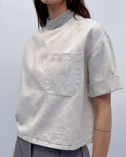 Person wearing an oversized light gray sweatshirt with a front pocket, rolled-up sleeves, and a sparkly silver turtleneck underneath.