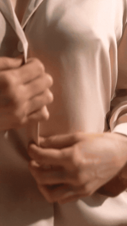 Person adjusting a beige satin shirt with their hands.