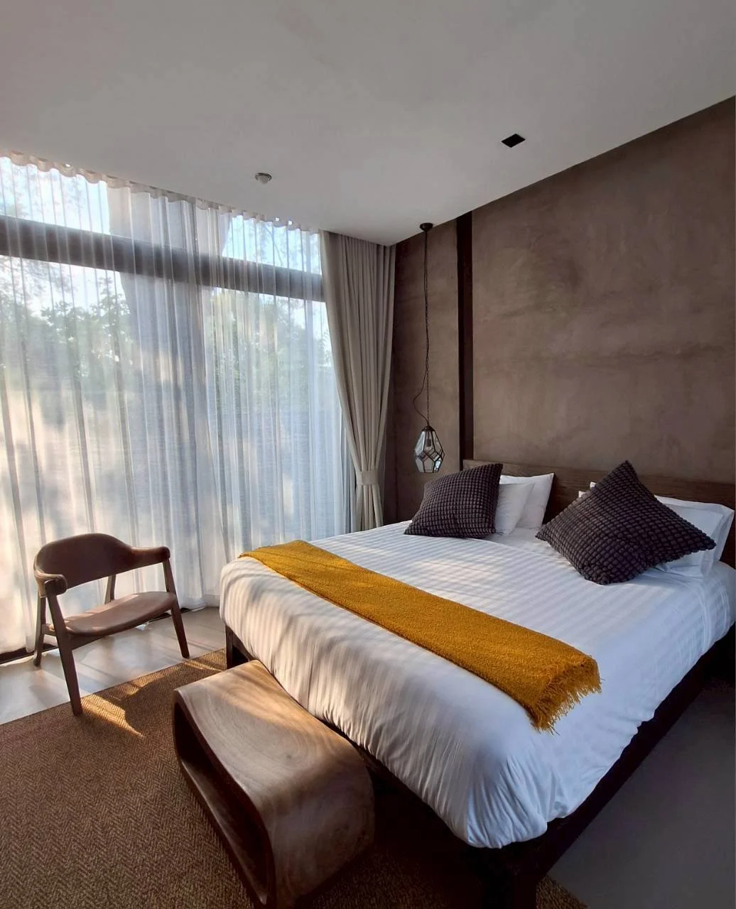 Modern Pool Access bedroom with a king size bed, a wooden bench at the foot, a brown chair, and sheer curtains letting in natural light within steps to outdoor swimming pool.