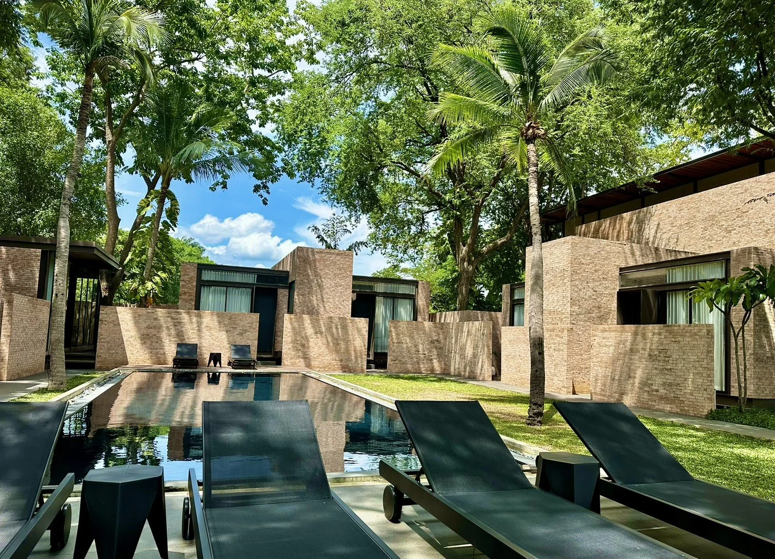 Luxury modern hotel with outdoor pool surrounded by trees and lounge chairs by riverside of River Kwai.