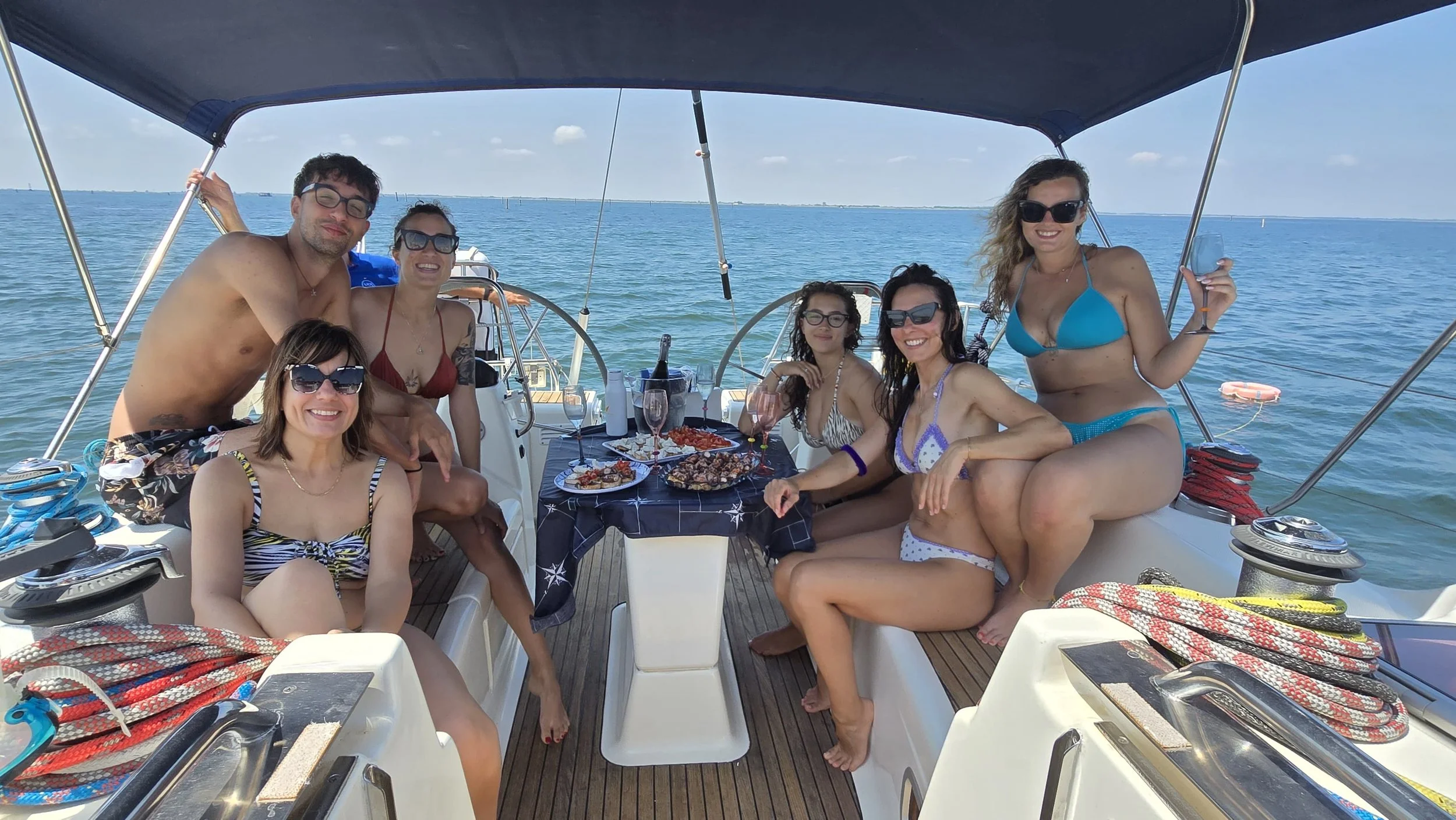 Gruppo di persone che si rilassano e mangiano sulla barca in mezzo al mare in una giornata soleggiata.