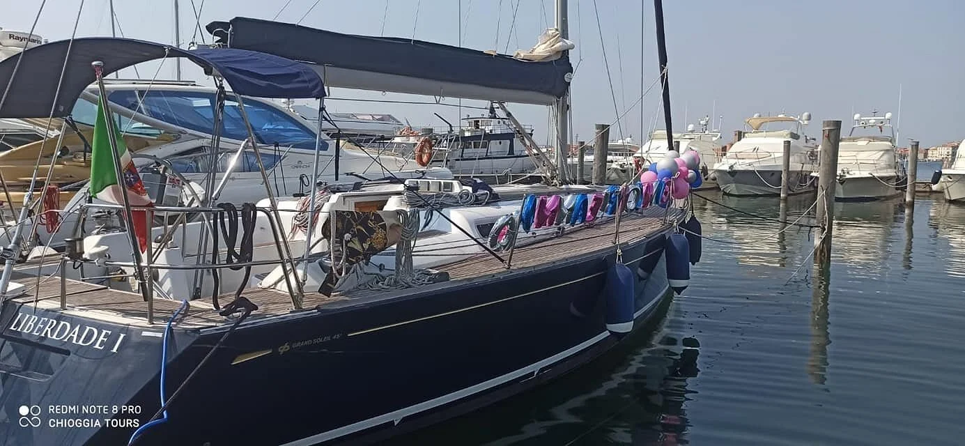 Motonave ormeggiata in un porto, con altre barche e yacht in acqua e strutture portuali sullo sfondo.