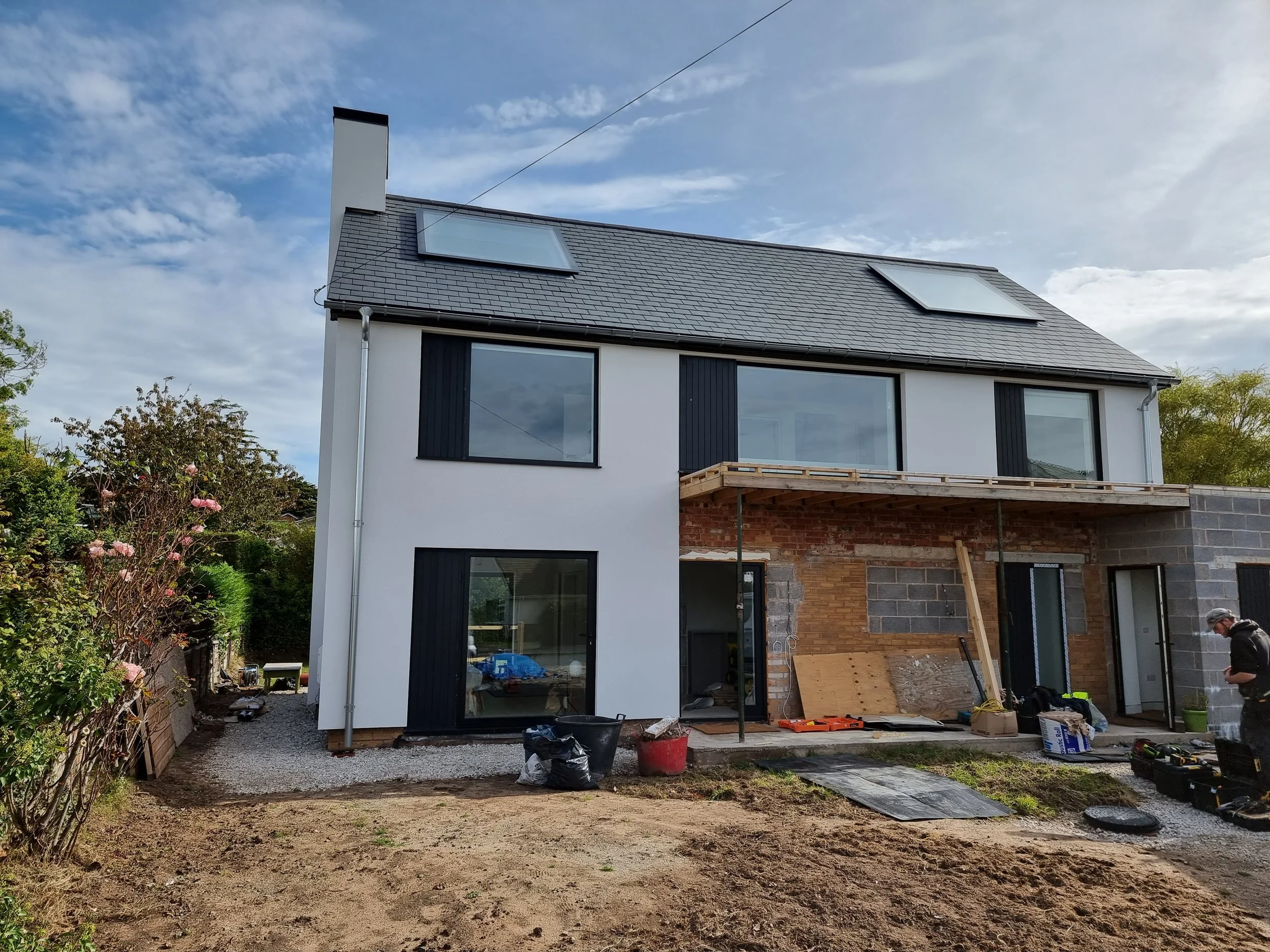 Construction site of a modern, white, three-story house with large windows and a black roof, external wall insulation, silicone render, K Rend render THIS
