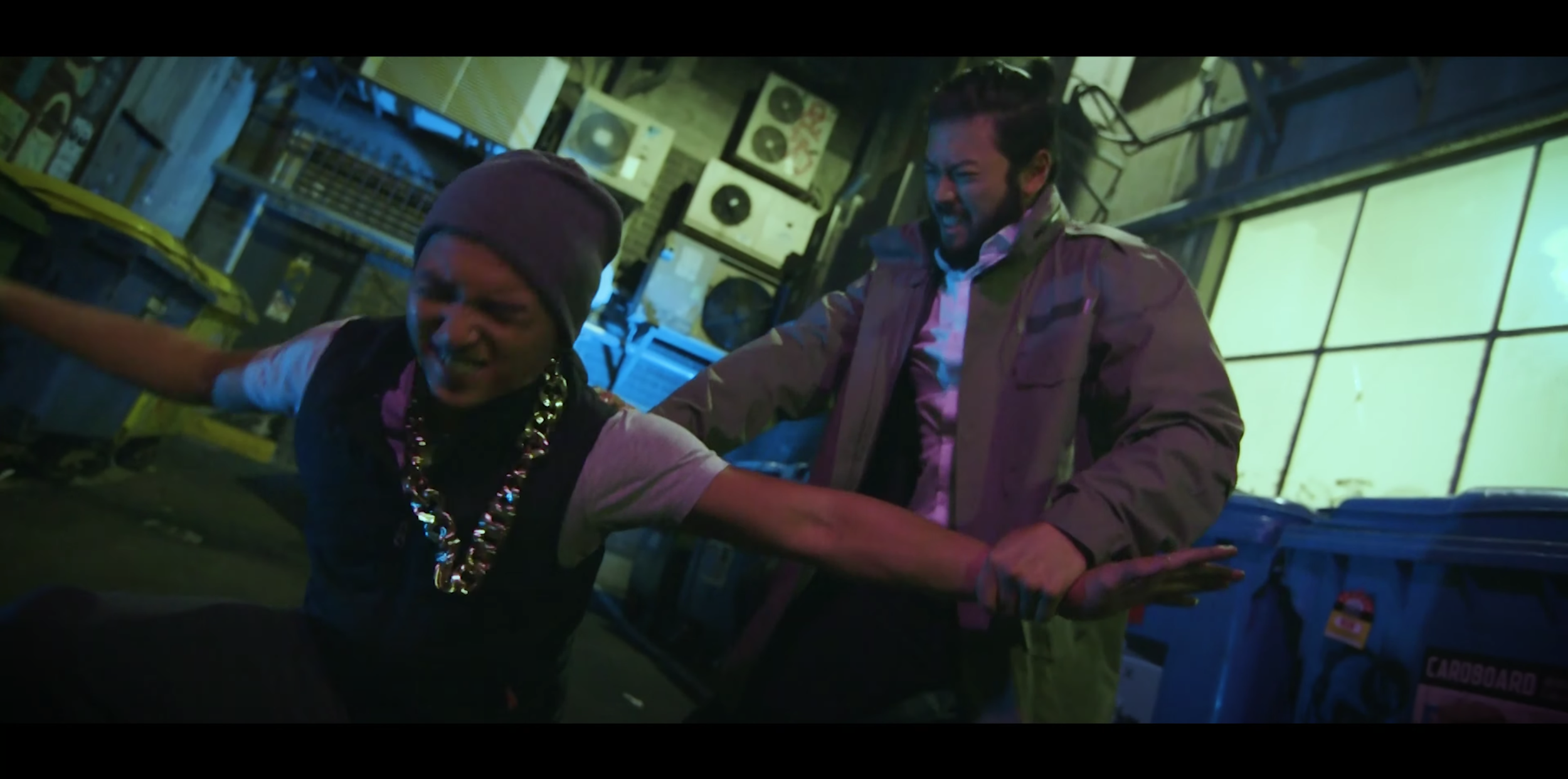 Two men in an intense fight inside a cluttered, dimly lit room with posters and records on the walls, and yellow and blue storage containers.