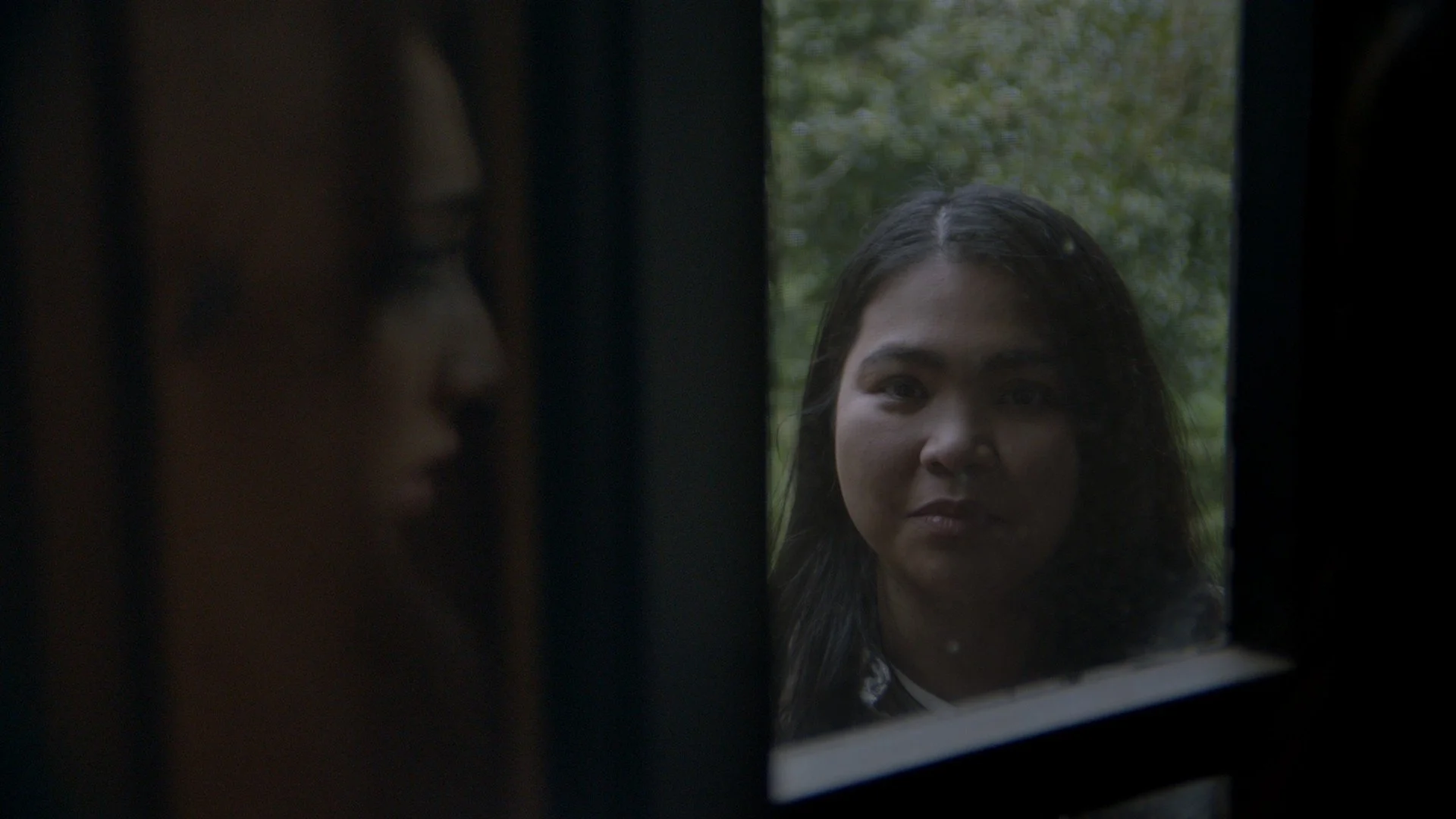 A woman looking through a window at another woman on the other side.