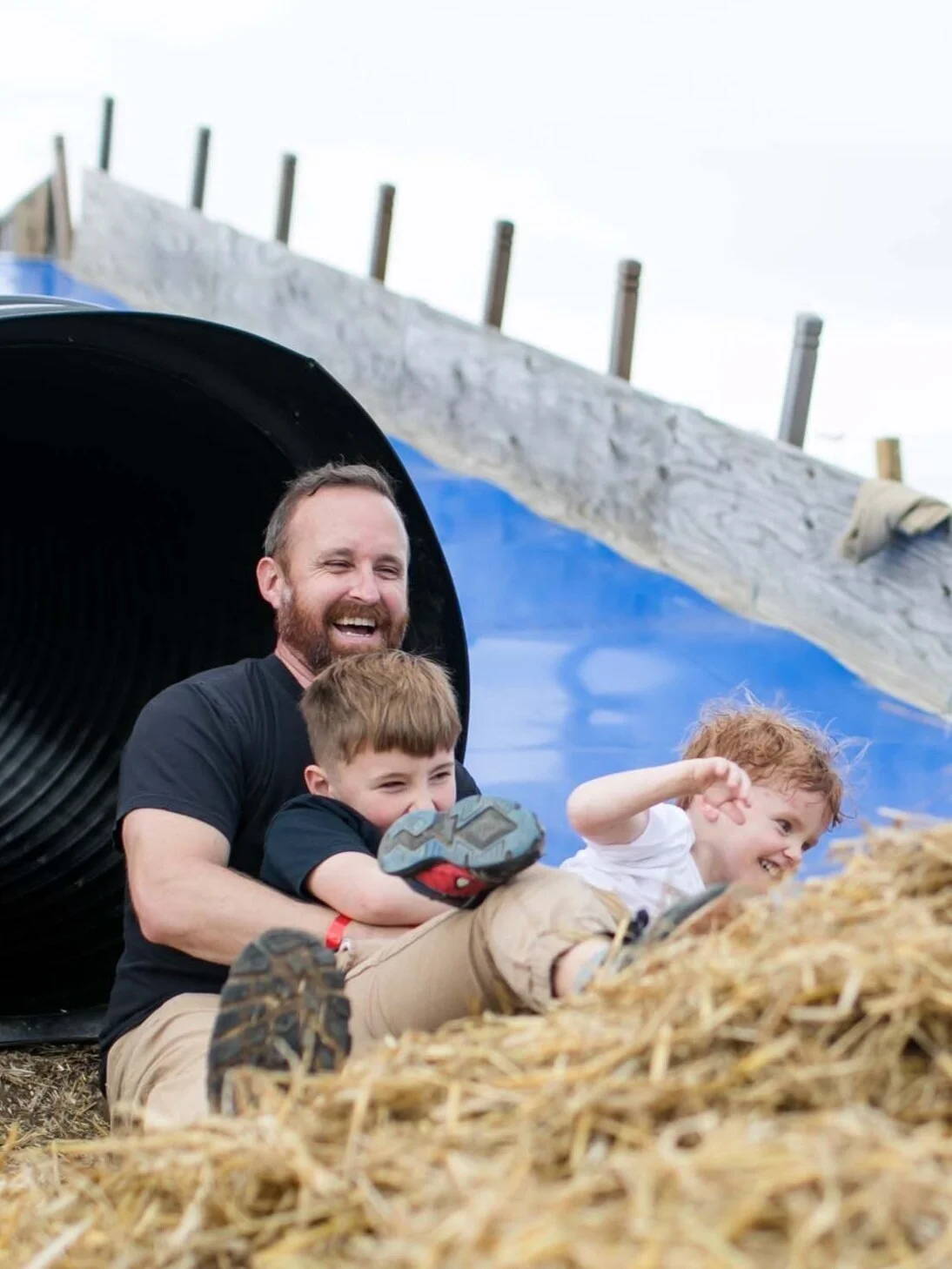 Happy Father and Two Sons Going Down Slide at Festival