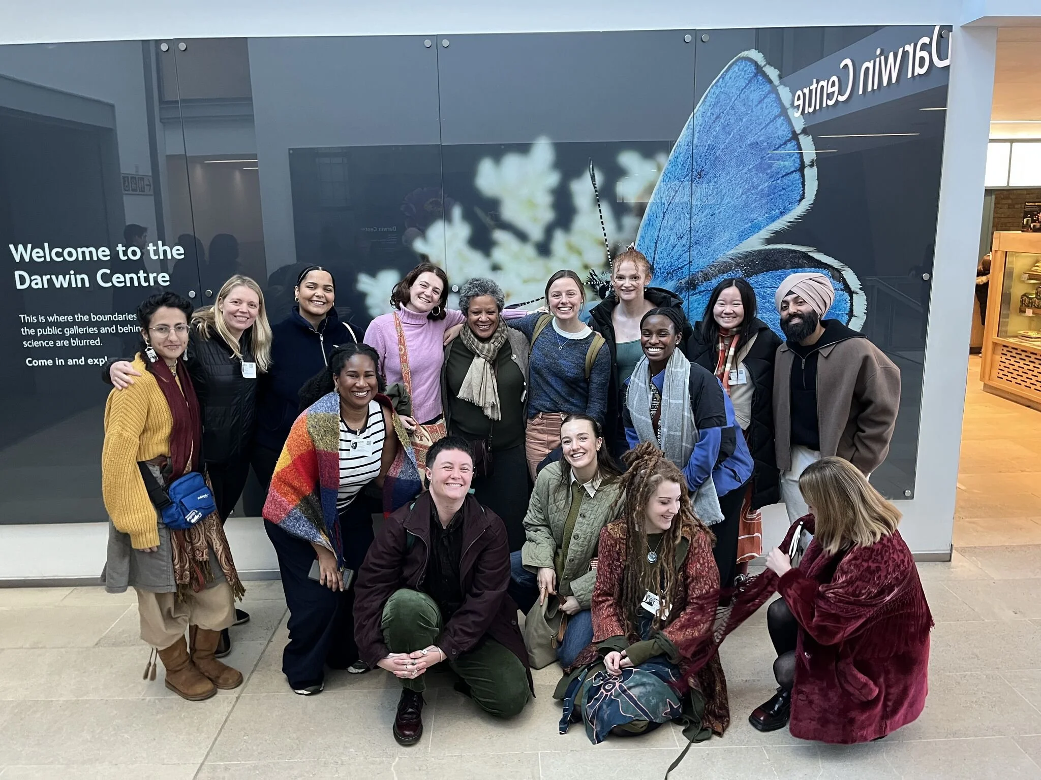 15 people posing for a photo at the Natural History Museum in London.
