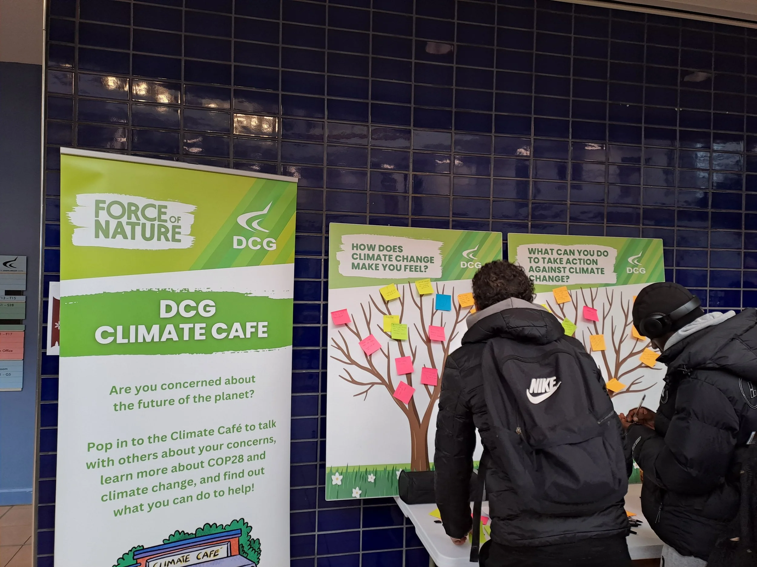 Two students stand in front of a board that says 'how does climate change make you feel?" writing responses on post-it notes.