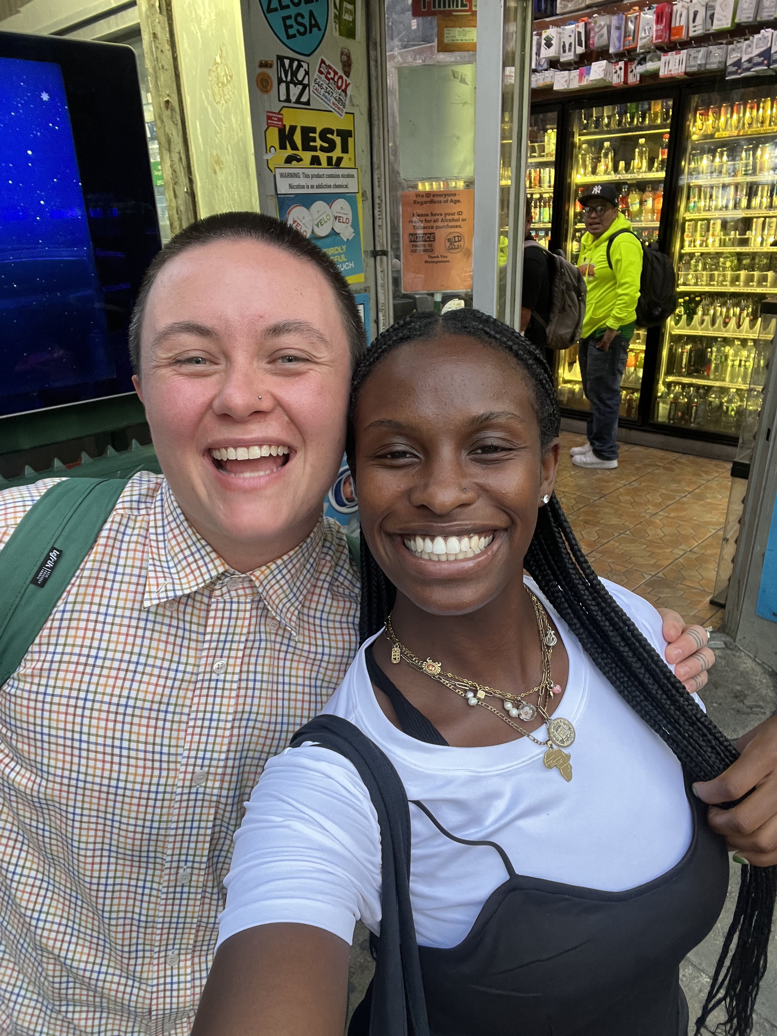 A white person with a shaved head and a black person with long braids are grinning whilst taking a selfie. 