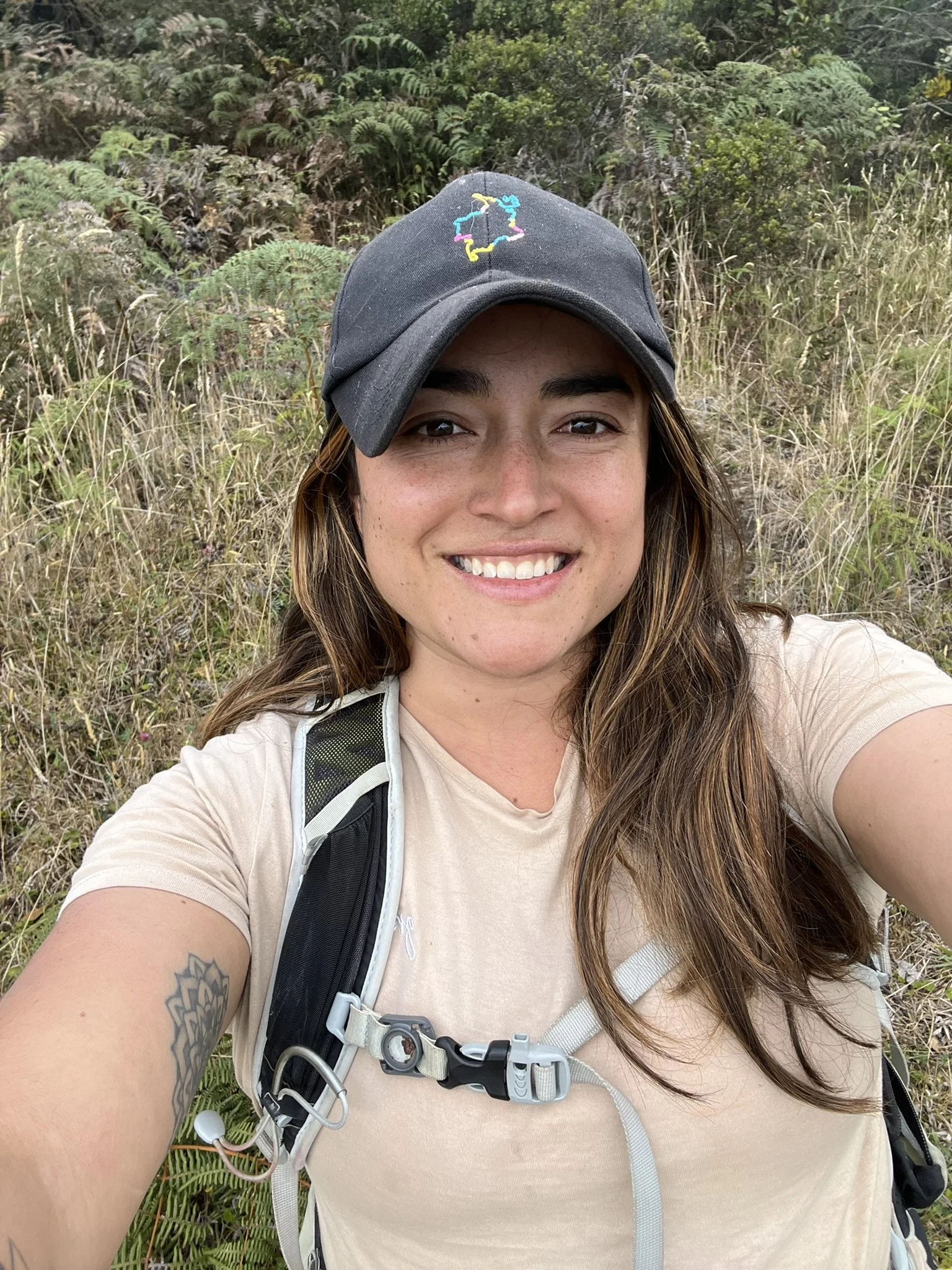 A woman with long dark hair is wearing a navy blue cap and smiling at the camera.