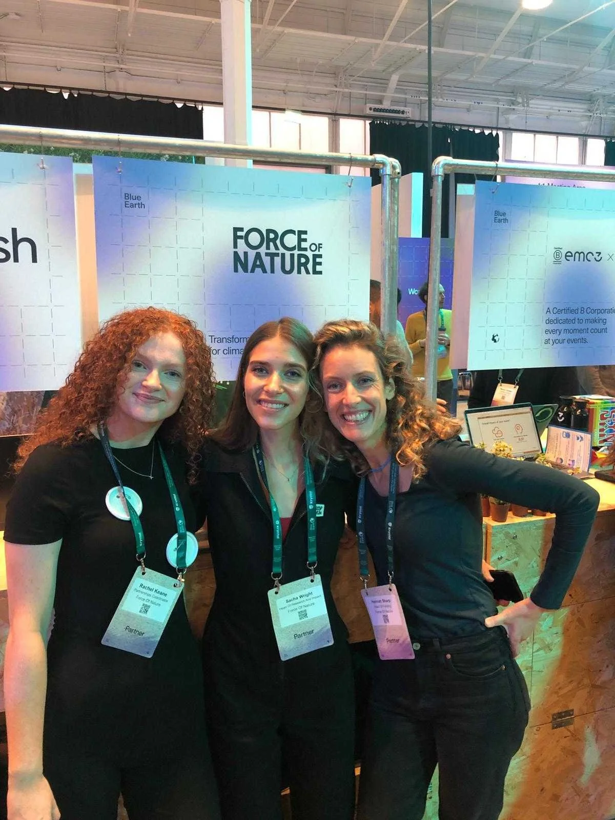 Three women standing side by side smiling in front of a Force of Nature branded poster