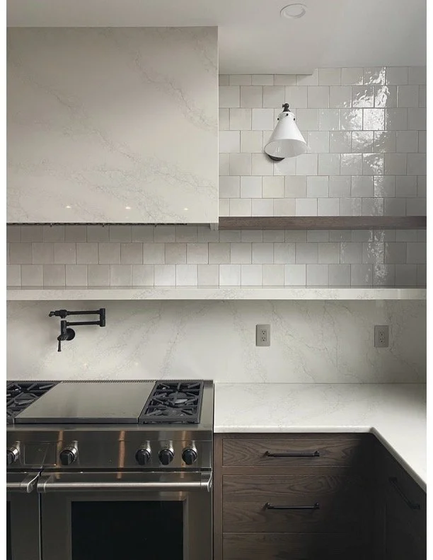 Modern kitchen with marble and tile backsplash, stainless steel stove, dark wood cabinets, and a white wall-mounted light fixture.