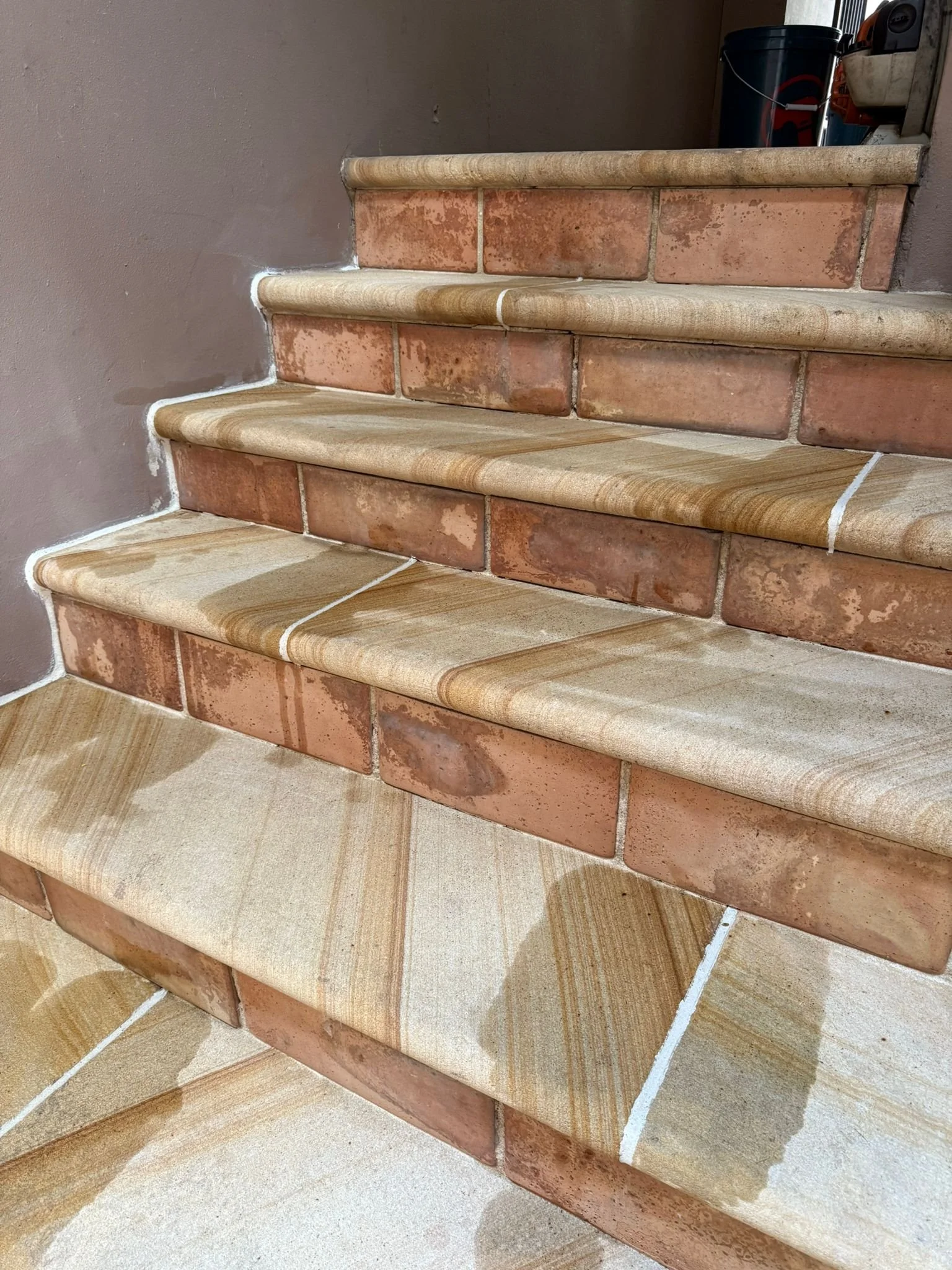 Photo of a staircase with terracotta tiles, light-colored rounded wooden trim, and beige tiled steps.
