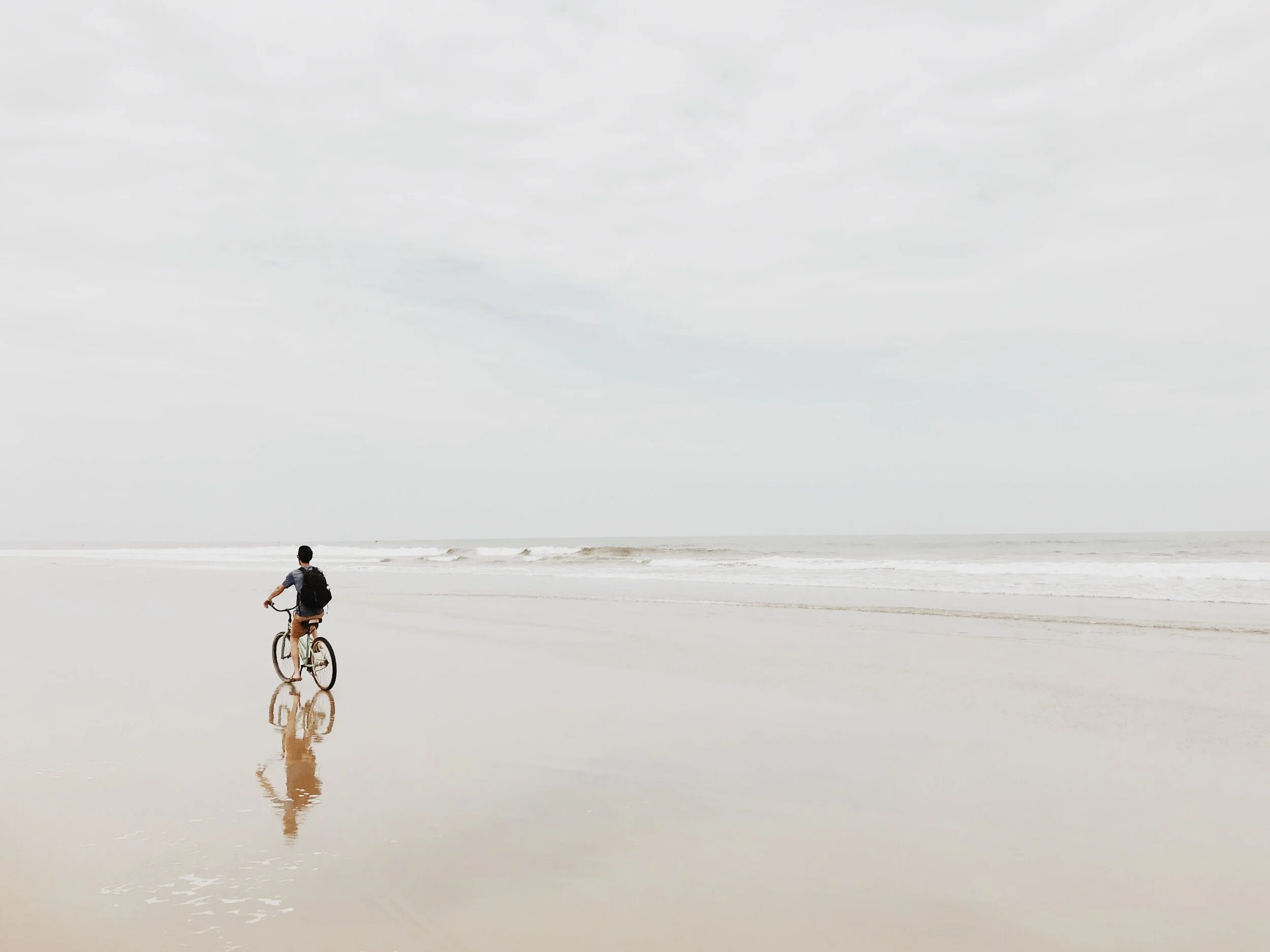 A person riding a bicycle along a beach with a cloudy sky and ocean waves in the background. White beach Ecuador