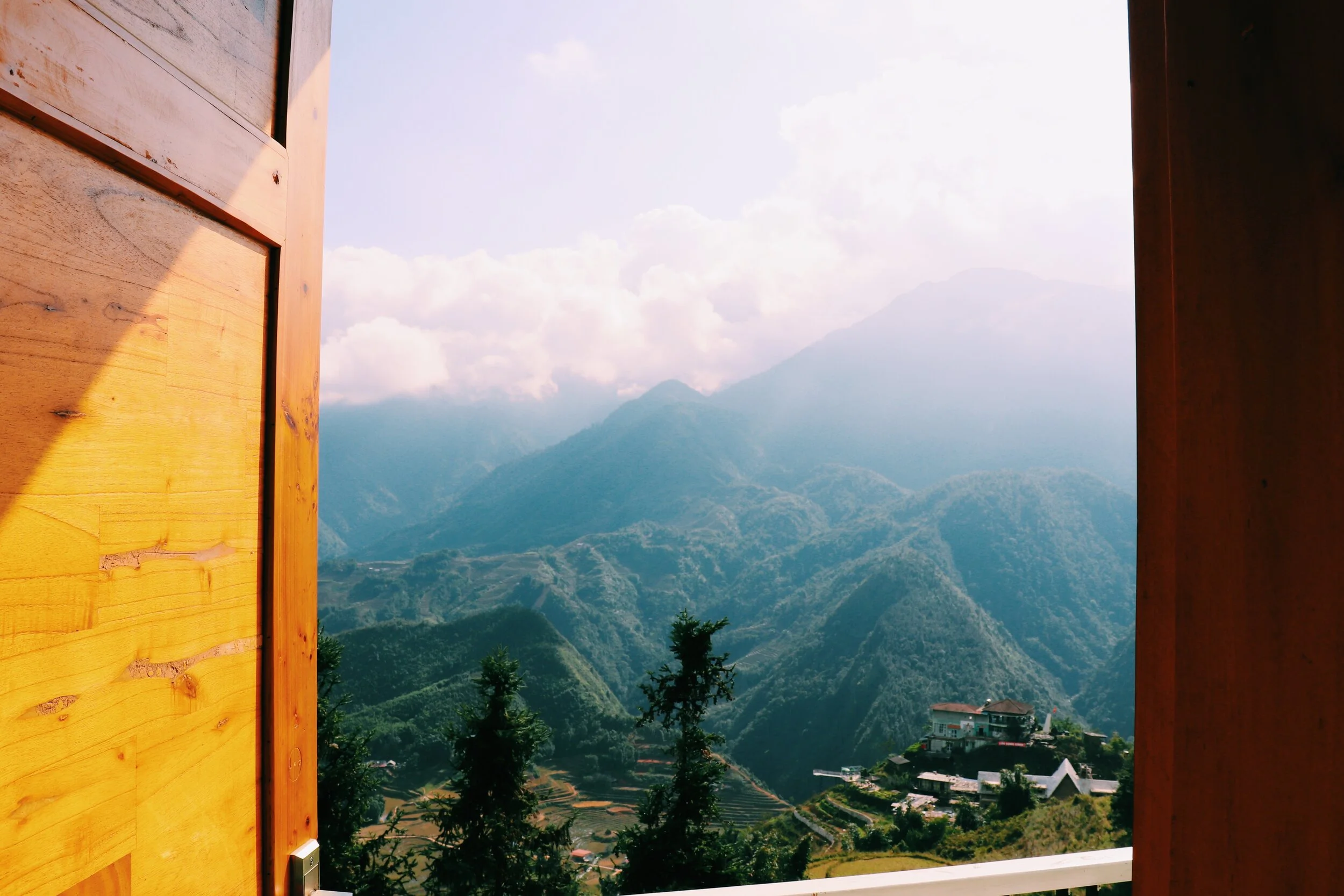 View of lush green mountains and valleys seen through a window with wooden frames, cloud-covered peaks in the distance. Sapa Vietnam