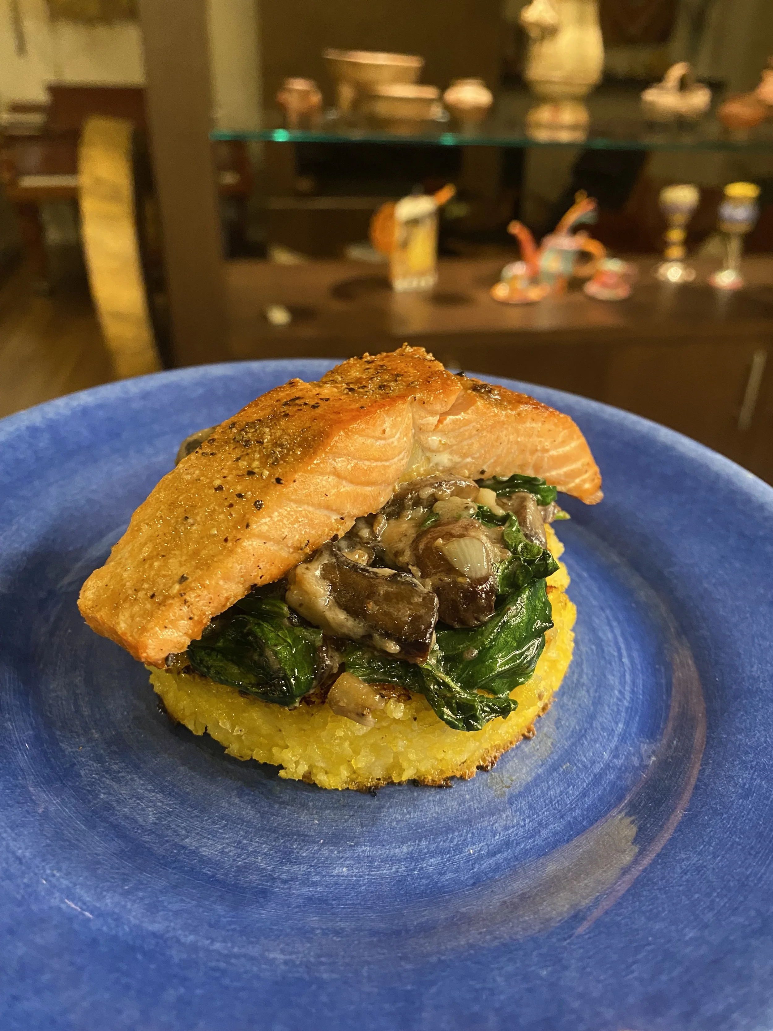 Private Chef in Aspen Colorado Roaring fork valley with A plated dish featuring a piece of grilled salmon on top of a bed of sautéed greens and mushrooms, served on a blue plate.
