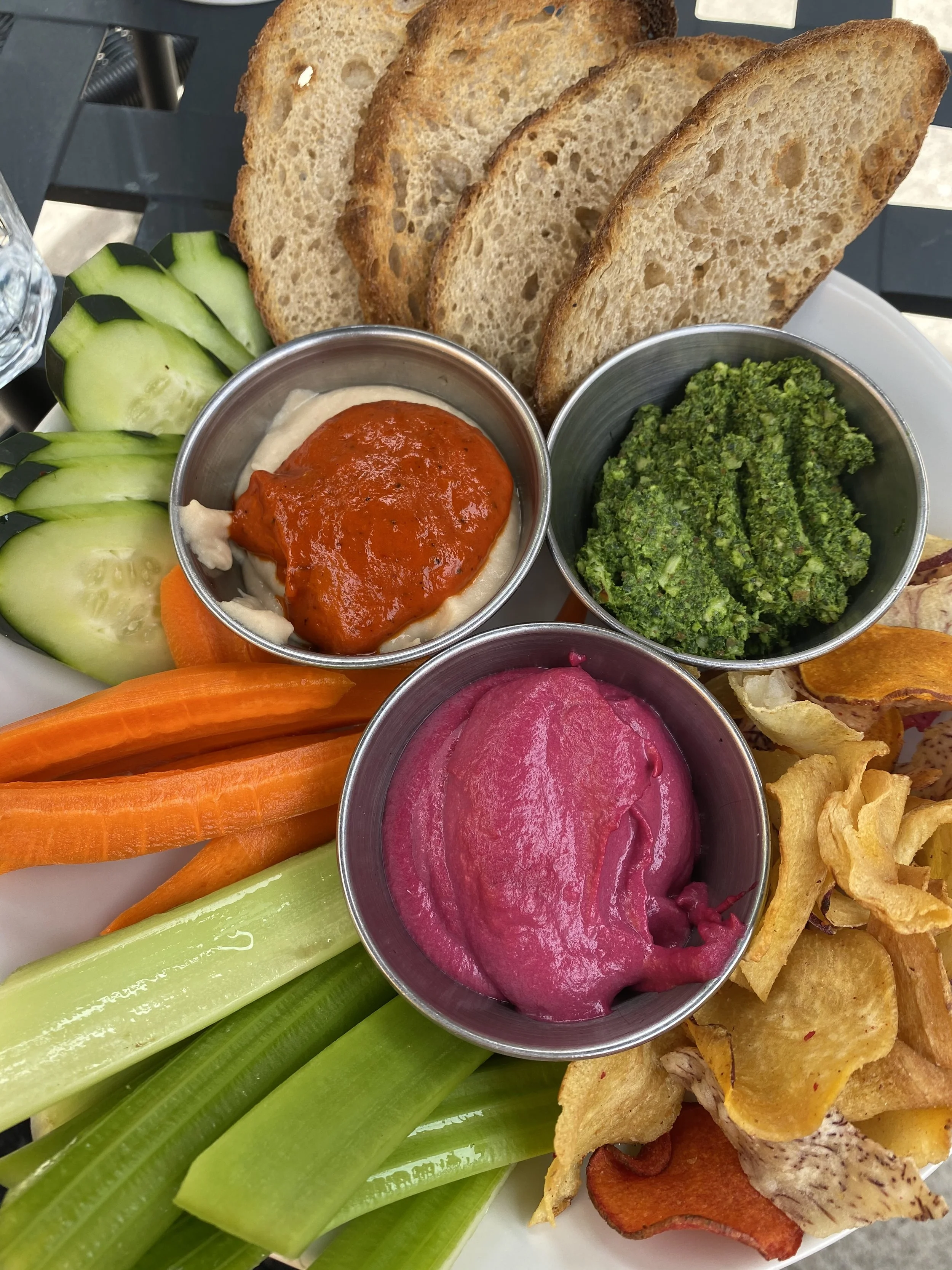 A platter of appetizers including sliced bread, cucumber, carrots, celery, beet hummus, green pesto, and vegetable chips. Private Chef in Aspen Colorado Roaring fork valley 