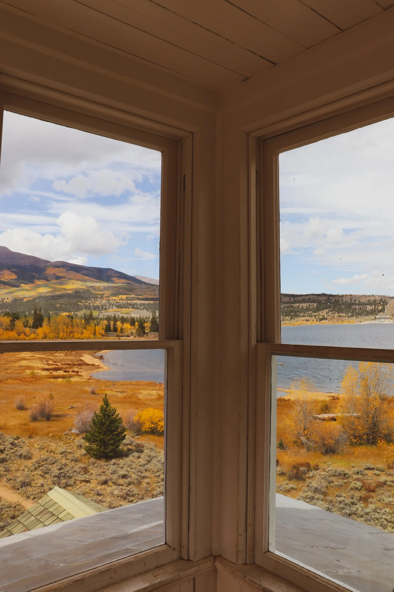 View through a corner of a window showing a landscape with trees, a lake, hills, and a partly cloudy sky. Twin Lakes Colorado Fall