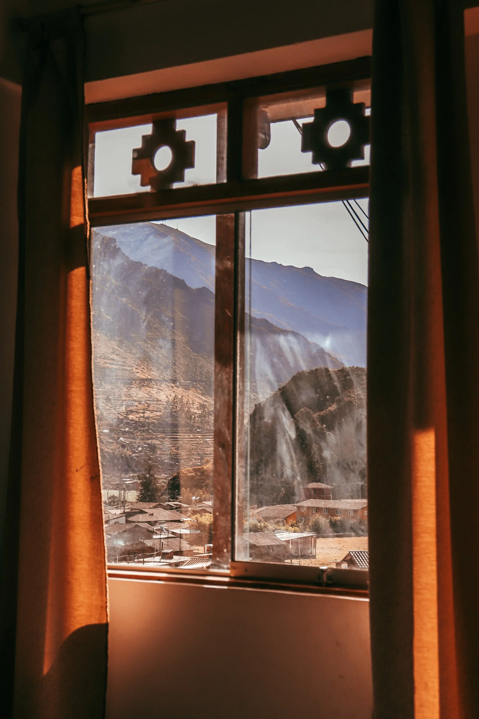 View of mountains through a window with brown curtains and decorative woodwork.