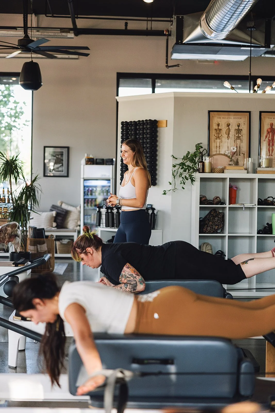 Fitness class inside a gym with women doing push-ups on mats, a trainer observing and smiling.