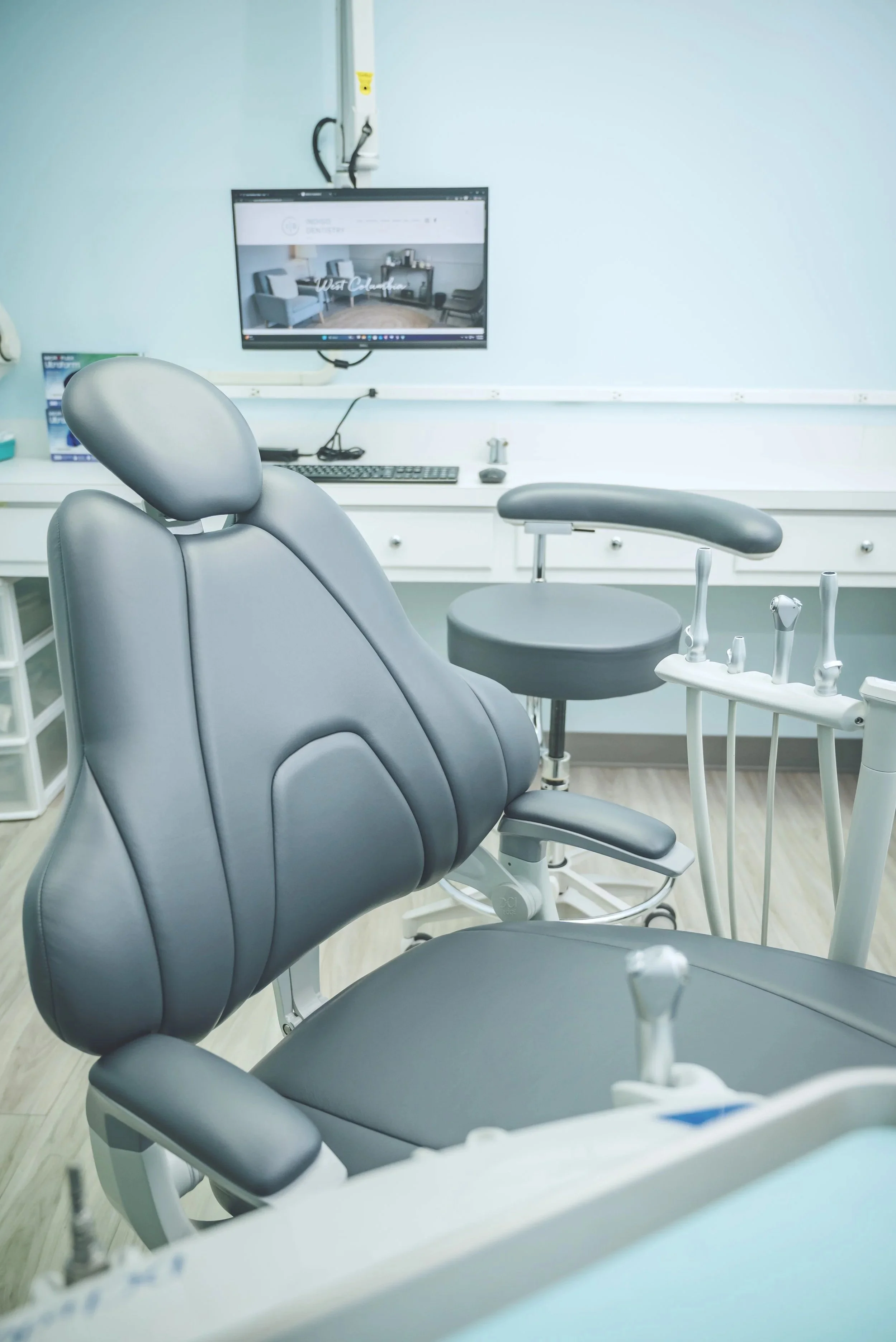 Dental examination room with dental chair, tools, and a monitor on the wall.