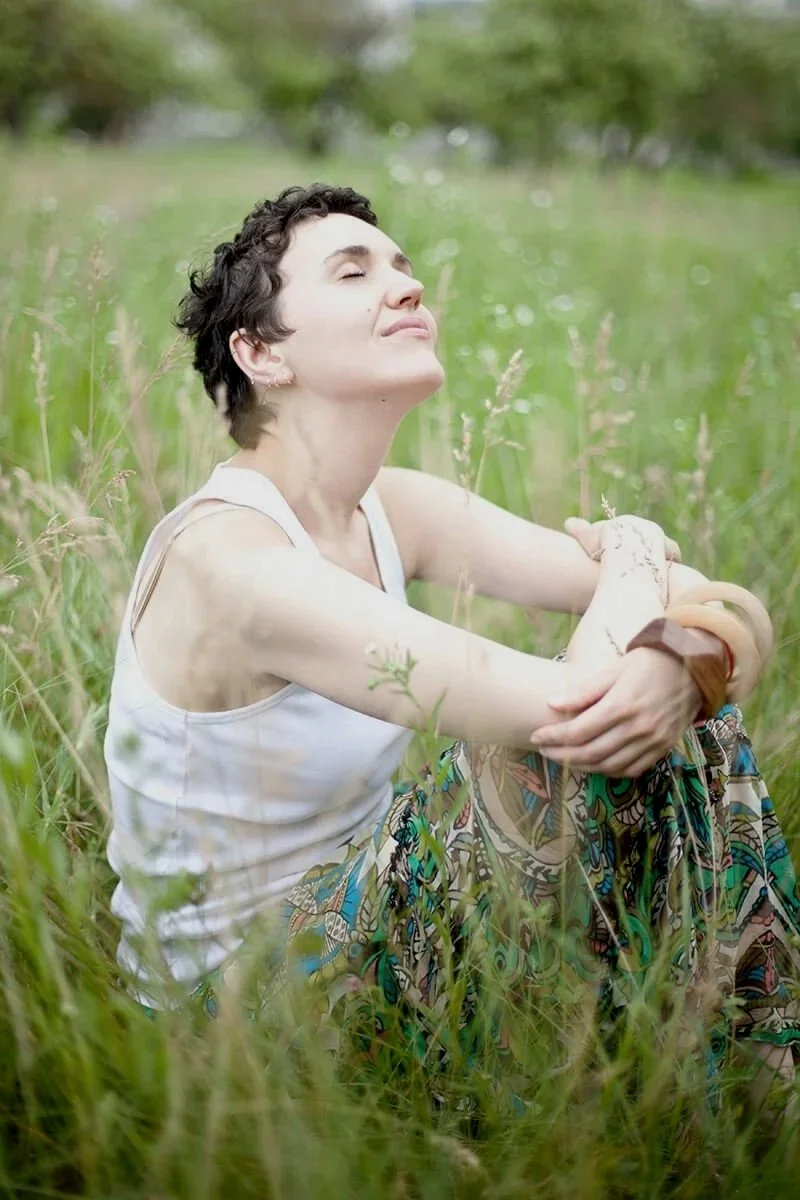 Woman sitting in a field, eyes closed and looking up, healing and refreshed