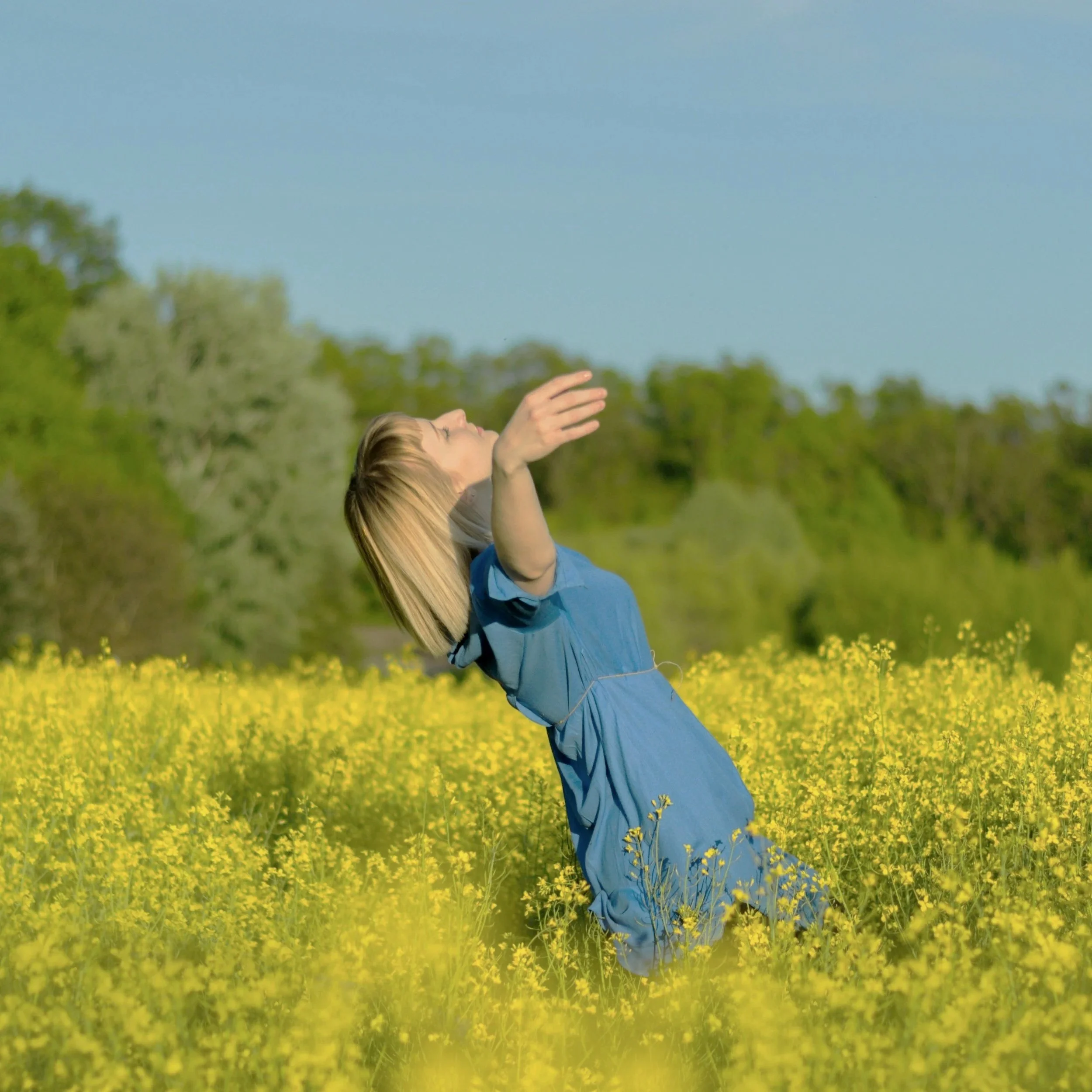 Woman in flower field, arms wide looking up at the sun feeling at home