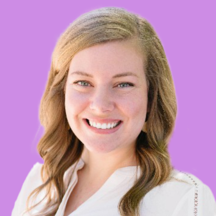 A blonde woman smiles at the camera. She wears a white collared shirt.
