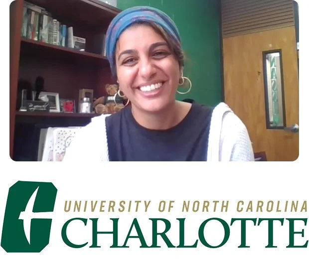 A light brown-skinned woman smiles at the camera. She has short black hair and wears a black shirt in front of a blue background above the University of North Carolina Charlotte name and logo.