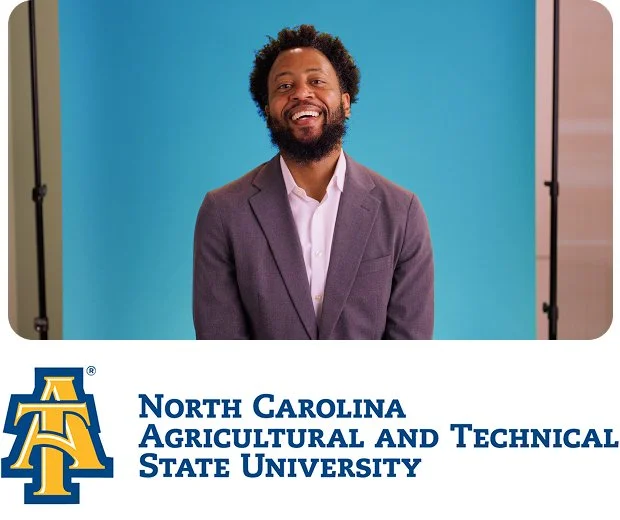 A black man with a short dark afro and fluffy dark beard wearing a blue shirt, white collared shirt, and yellow and black bowtie smiles at the camera in front of a yellow background with North Carolina Agricultural and Technical State University logo