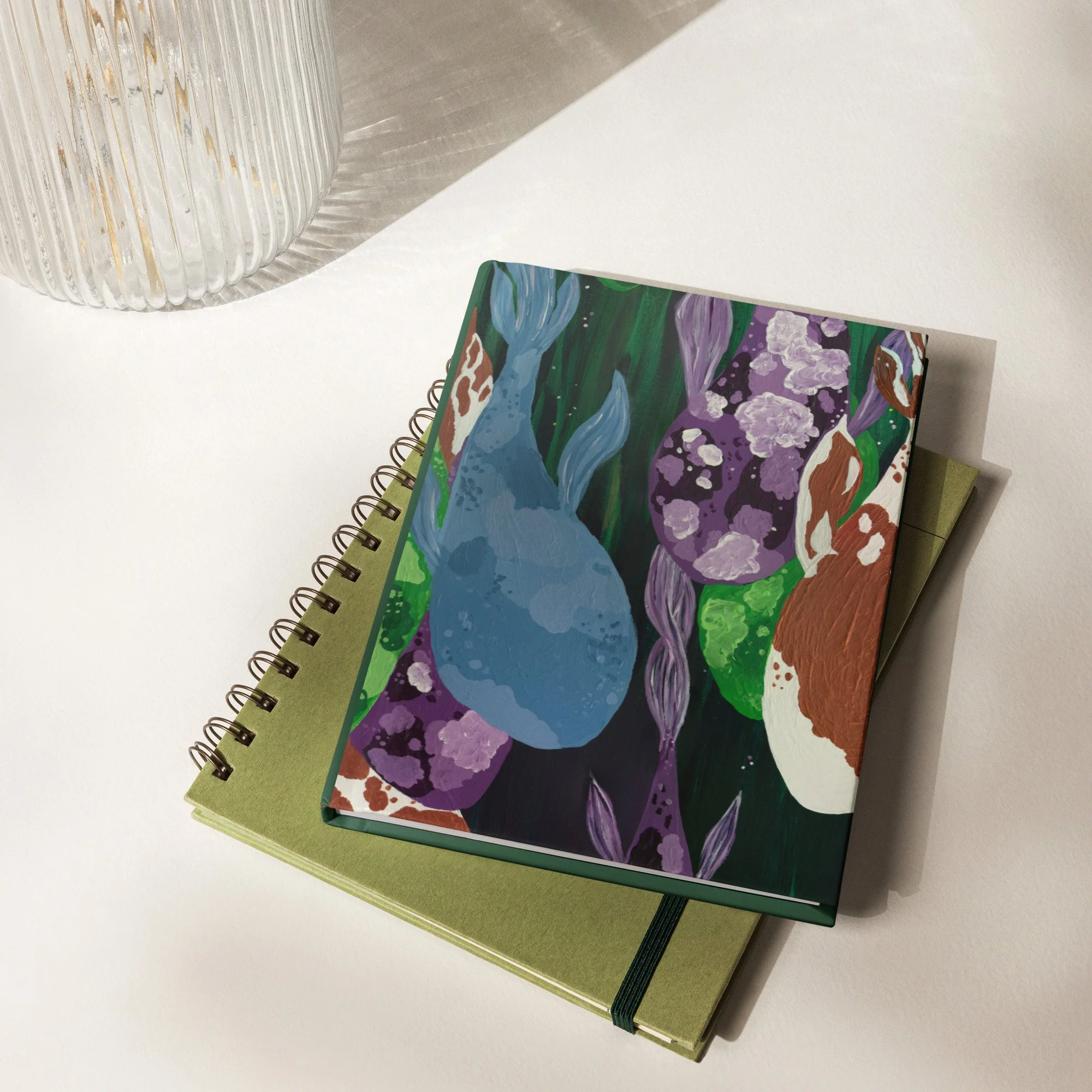 Flay lay of the hardcover journal on top of a spiral notebook on a desk.