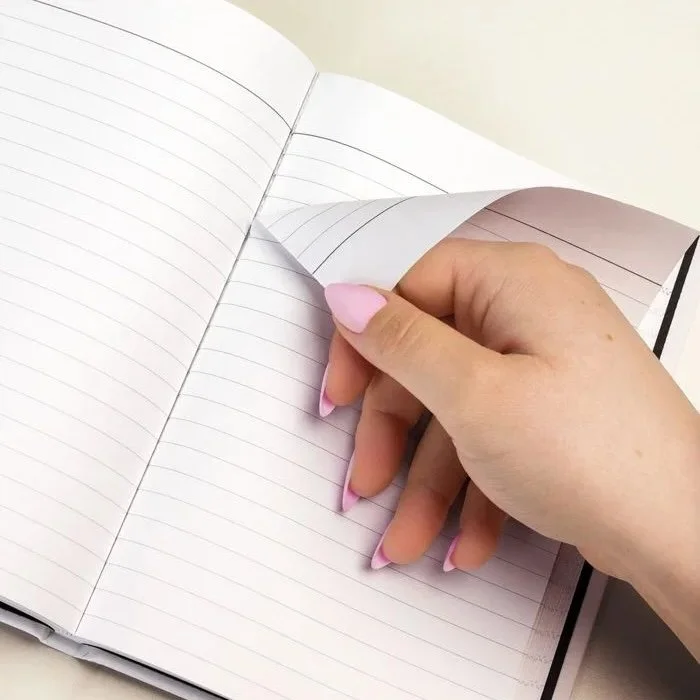 Flat lay of a hardcover journal with a human hand gently tearing out a perforated page.