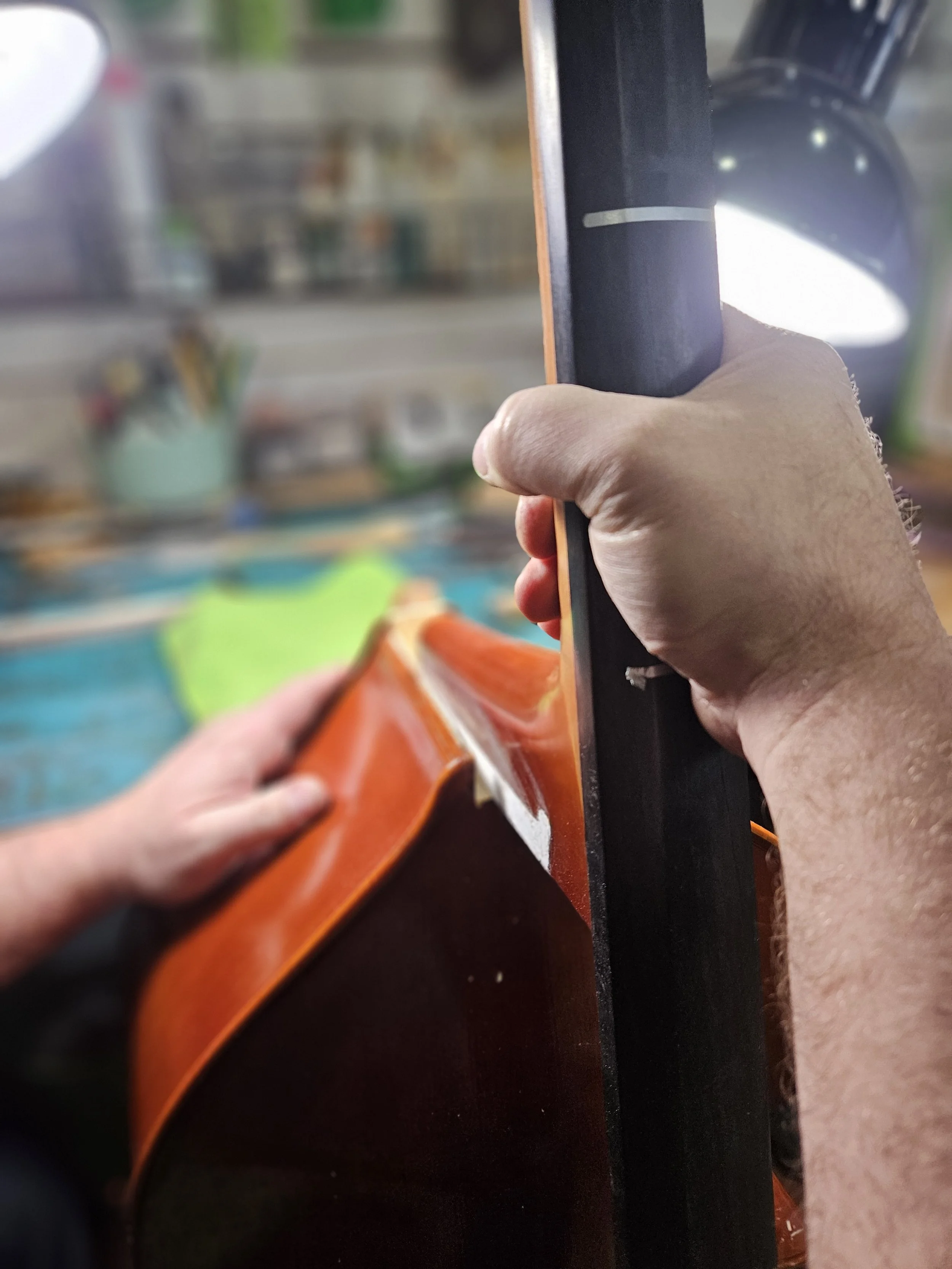 Person  installing the neck of a double bass into the body to repair the neck in a workshop.