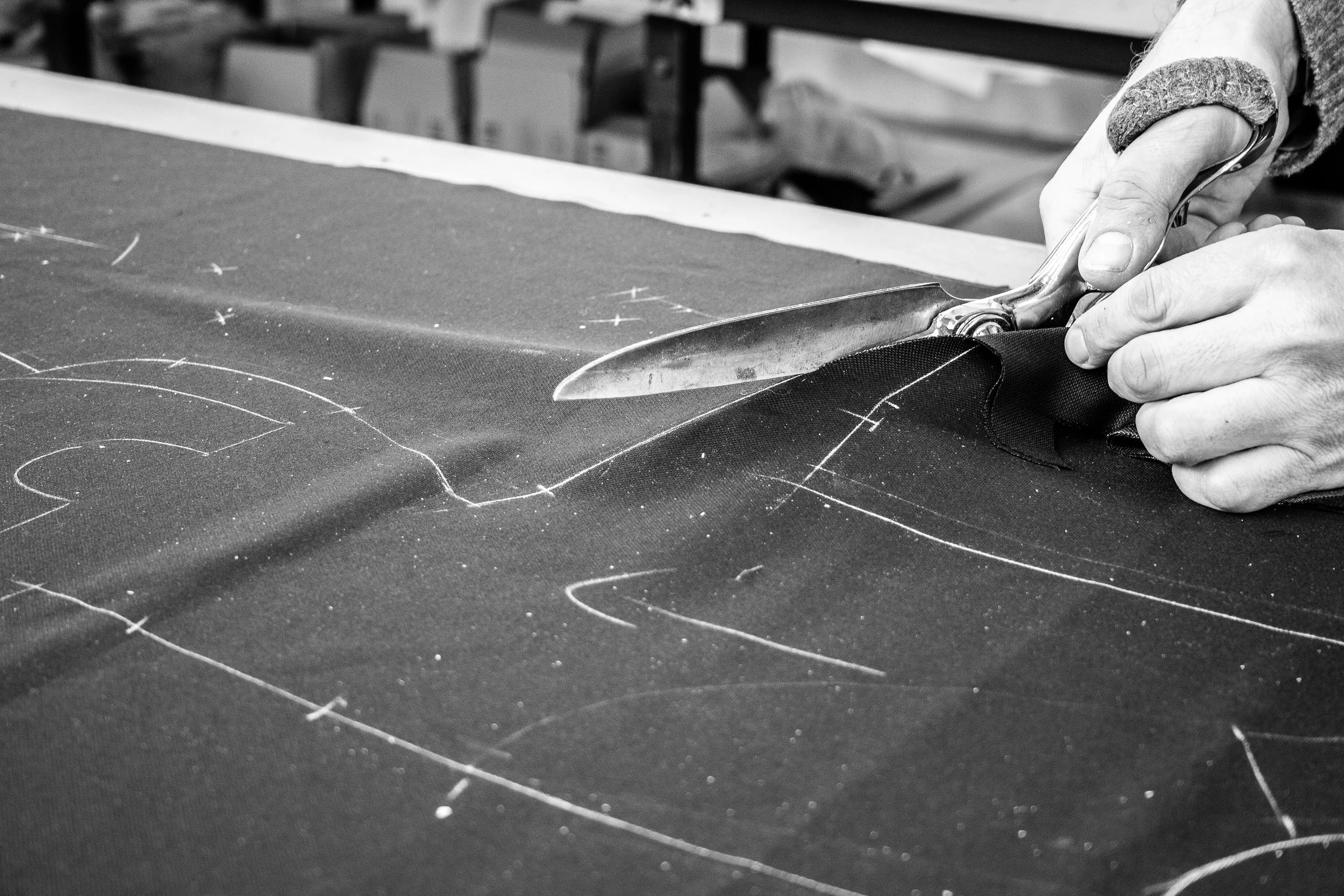 A person is cutting fabric with a pair of scissors on a worktable, with chalk markings visible on the fabric.