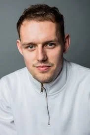 Young man with short brown hair and slight smile wearing a white zip-up jacket, posed against a gray background.