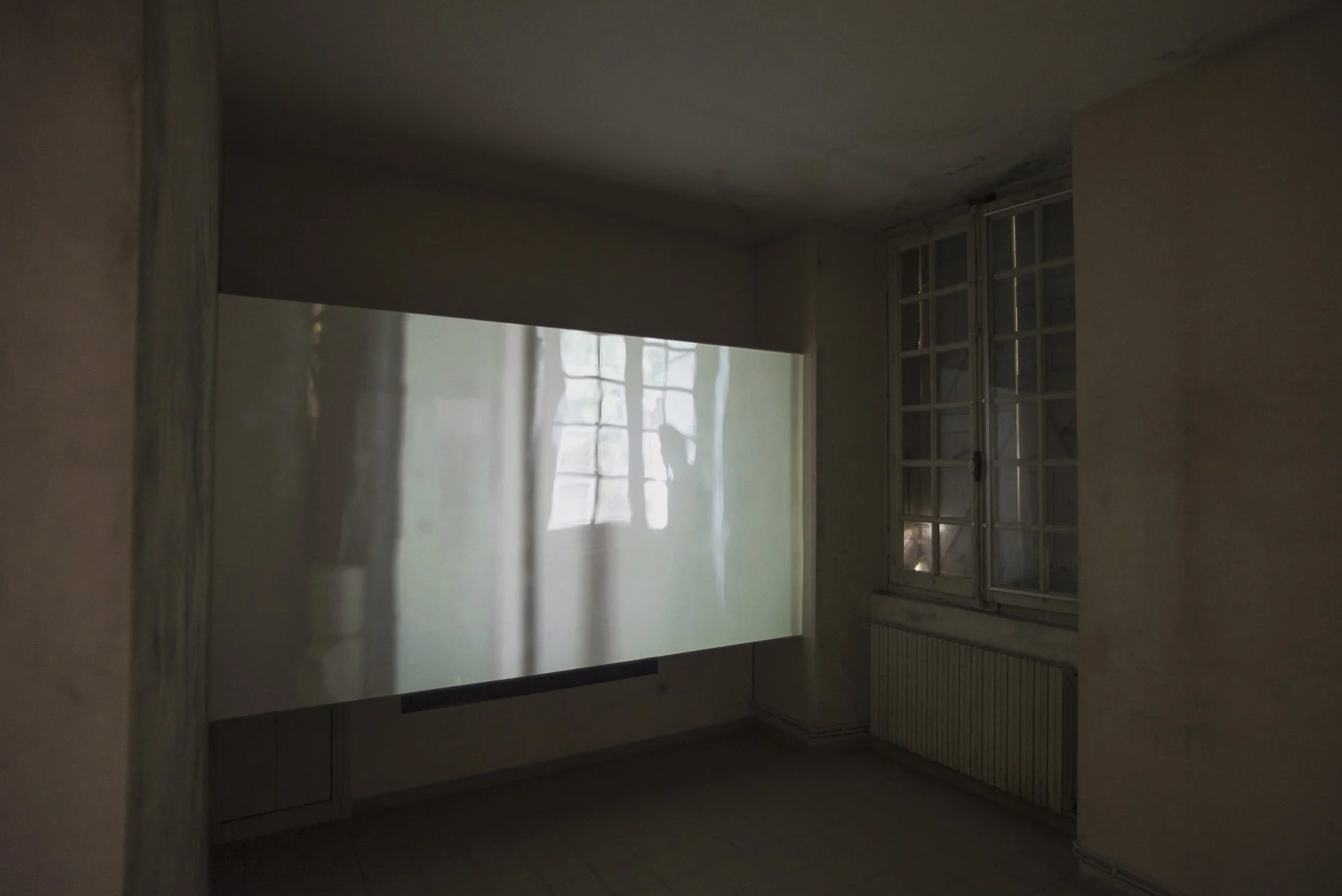 Empty room with a window and a projection on the wall showing a reflection of windows with grid panes.