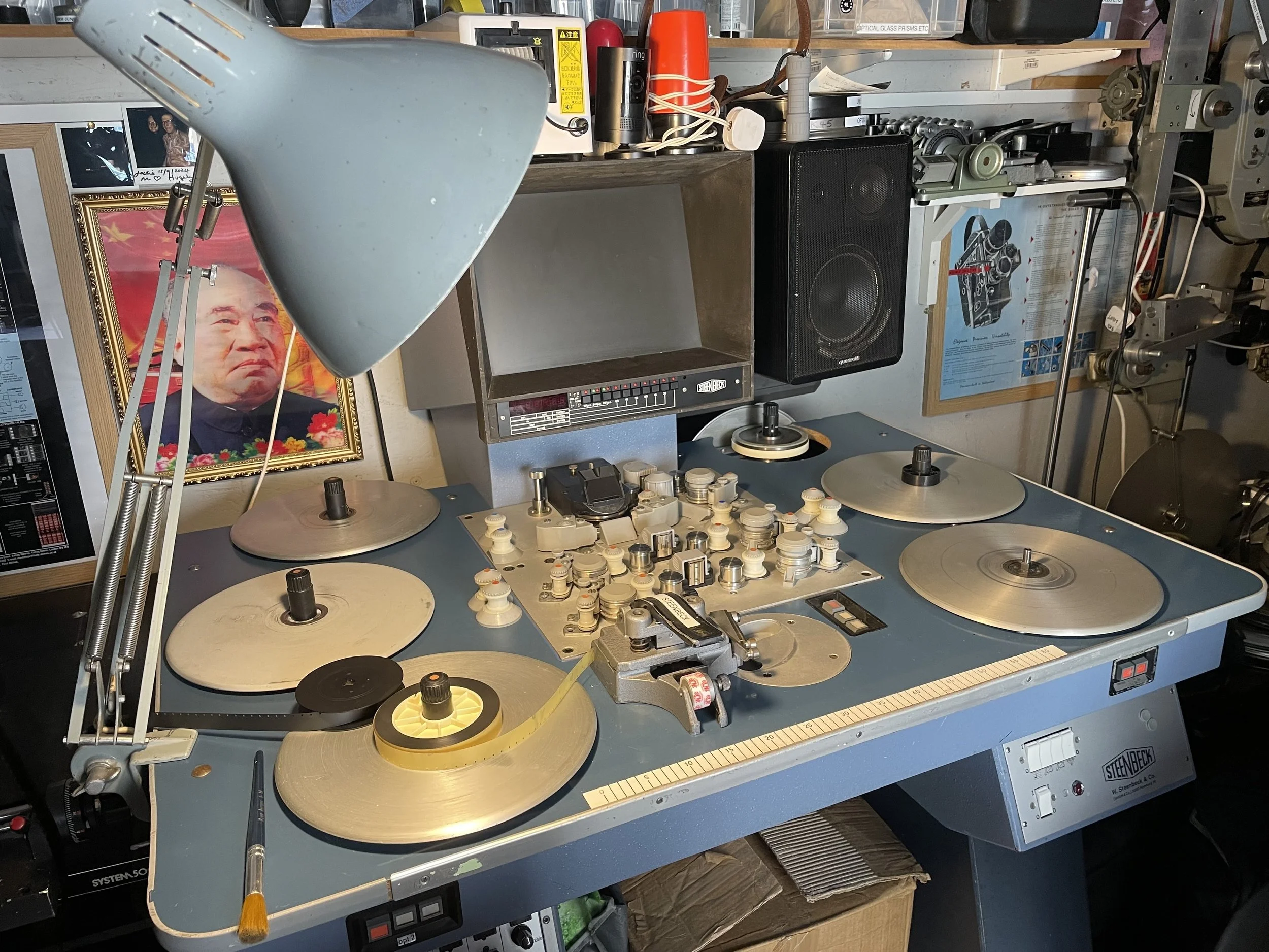 An old-fashioned DJ turntable and mixing desk with several records, a lamp, and a wall framed photo of Mao Zedong in the background.