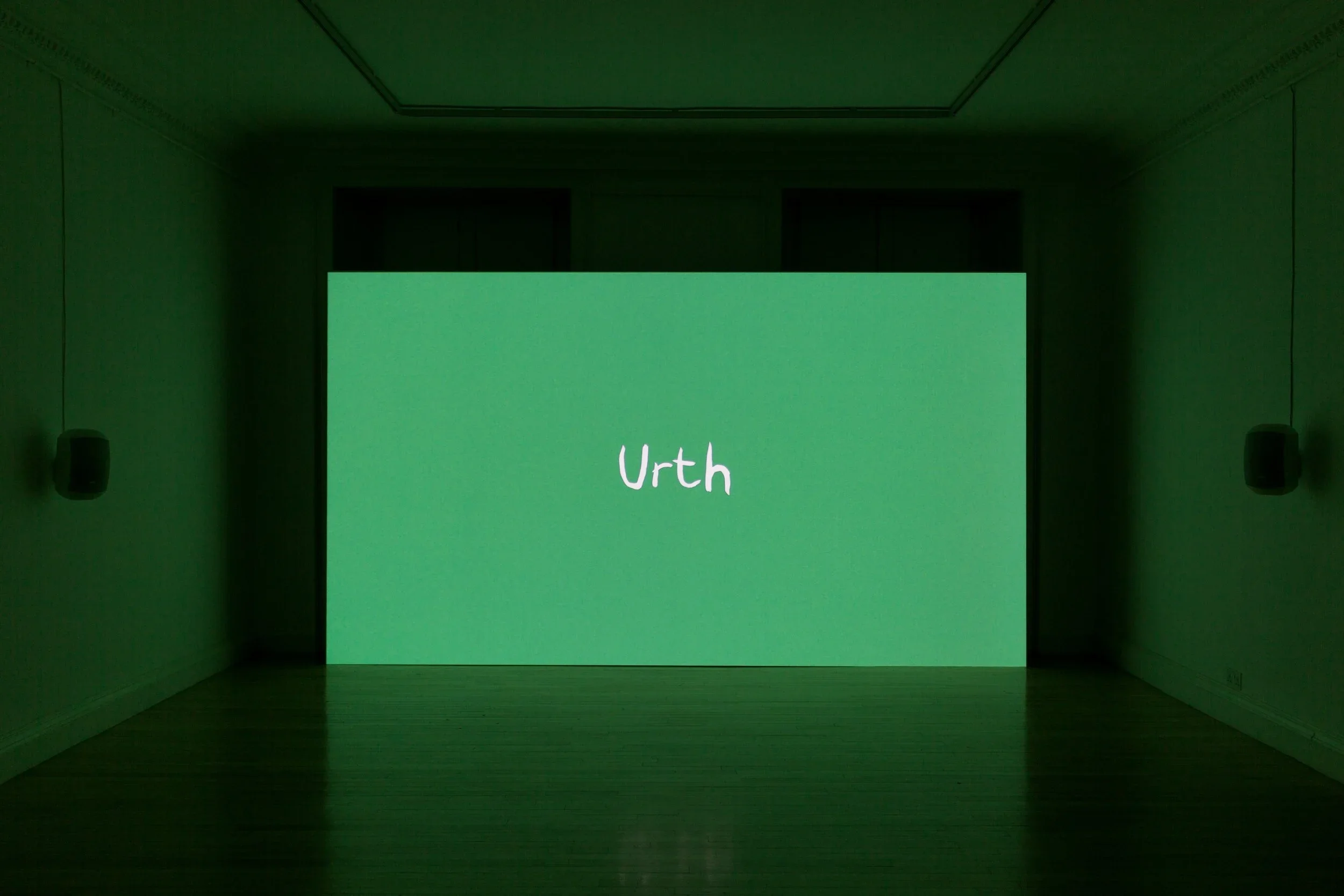A green screen with the word 'Urth' written on it in a dimly lit room.