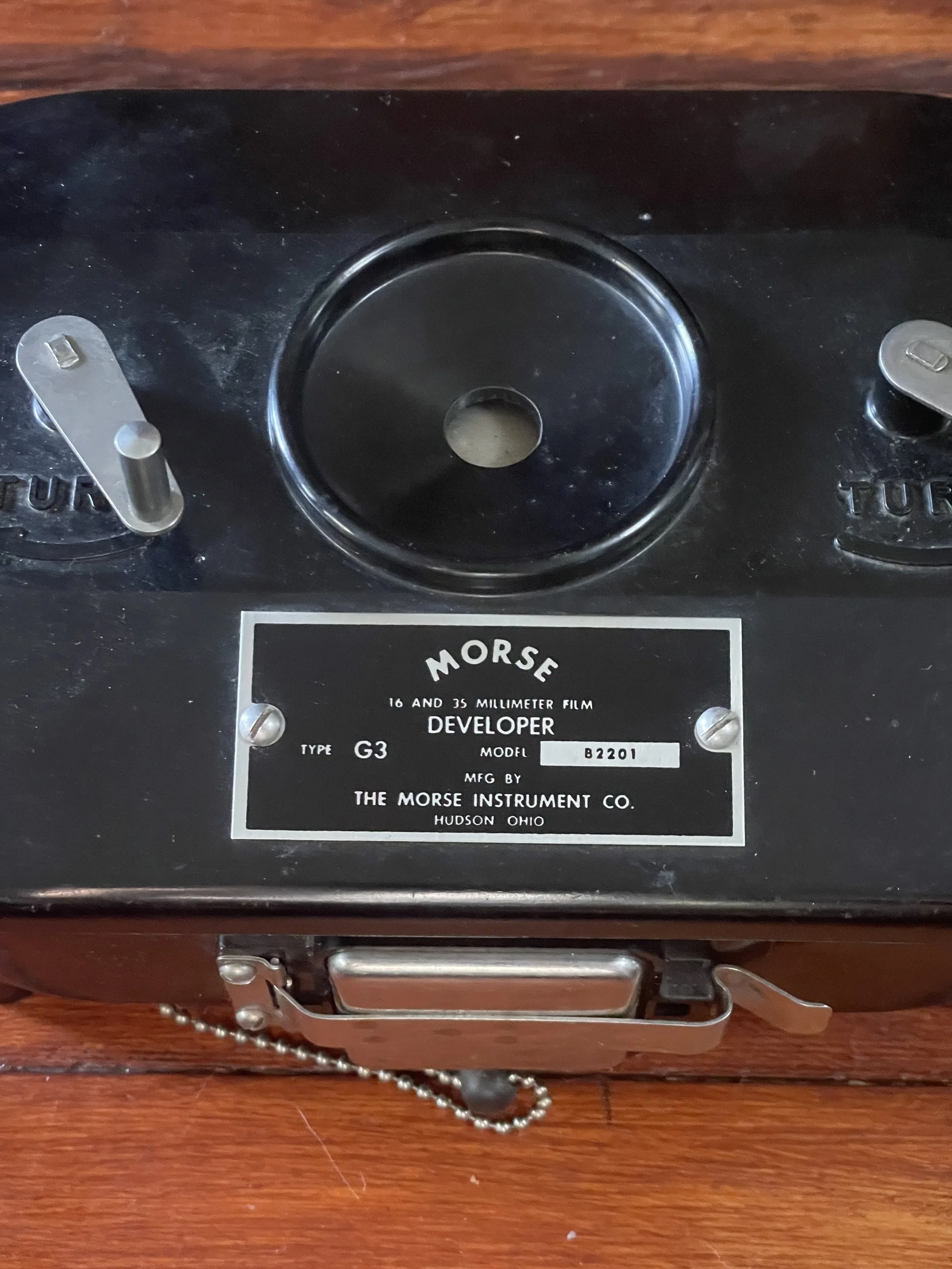An old Morse developer device with a black metal base, a circular indentation at the top center, and metal switches on the left and right sides. There is a label beneath the indentation that reads: MORSE 16 AND 35 MILLIMETER FILM, DEVELOPER, TYPE G3,
