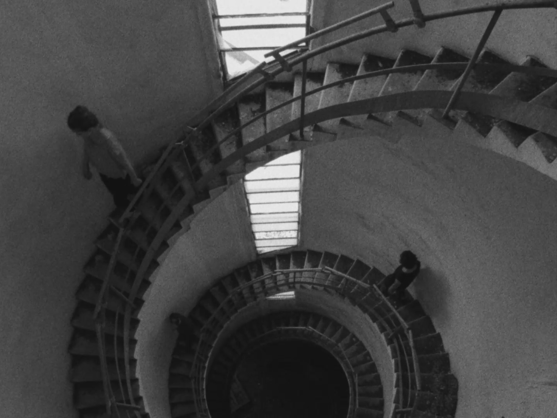 A black and white photo of a spiral staircase viewed from above with three people walking on the stairs.