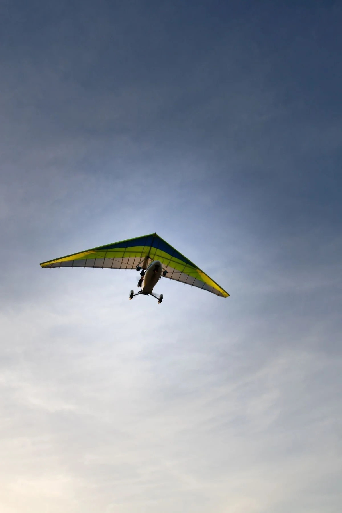 A small aircraft with yellow, green, and blue wings flying in a cloudy sky.