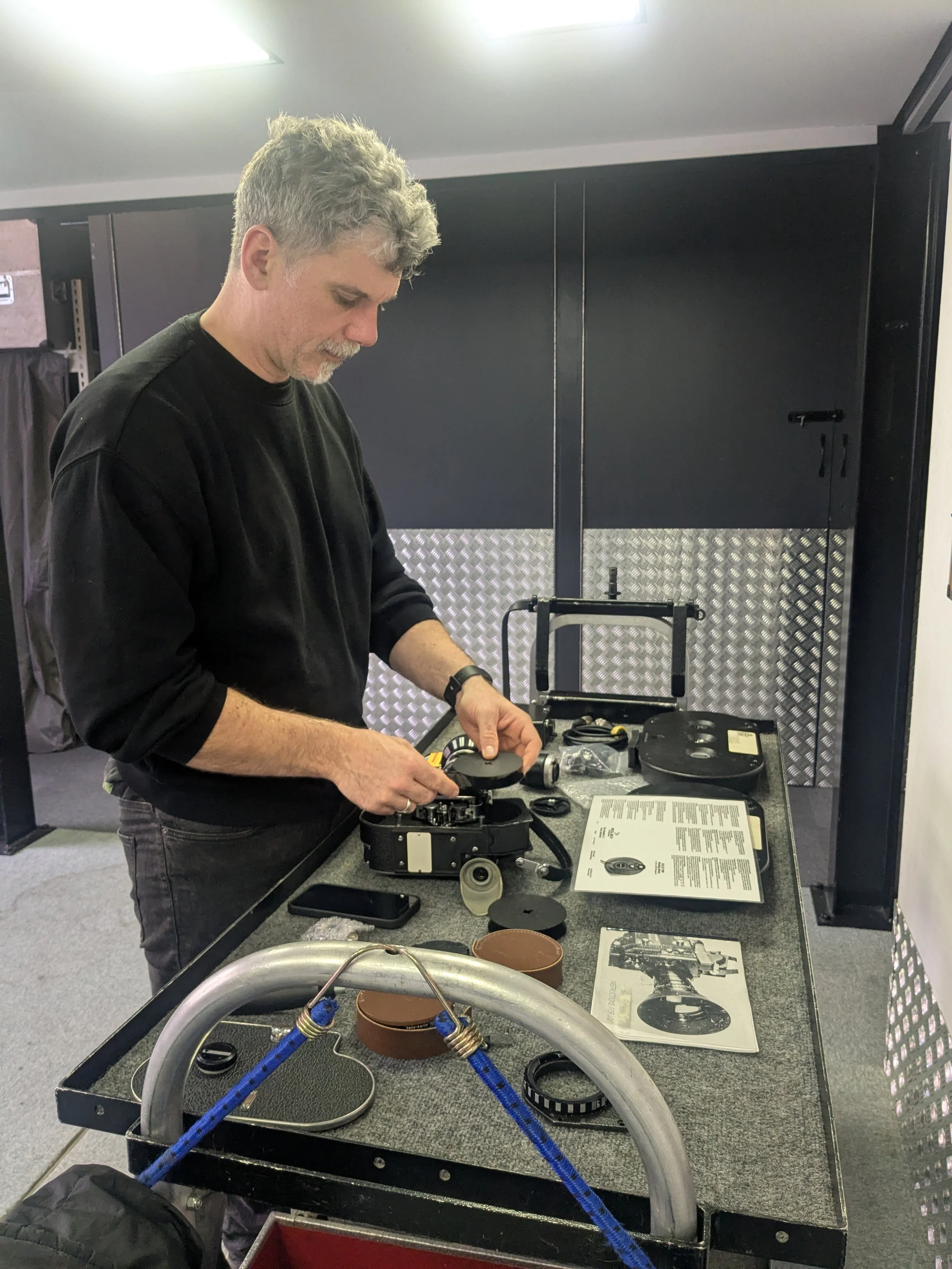 A man working on a vintage camera or projector on a worktable in a workshop or repair shop.