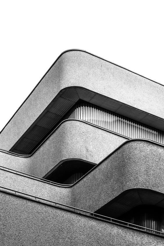 Close-up of modern, concrete building with rounded edges and dark window frames in black and white.