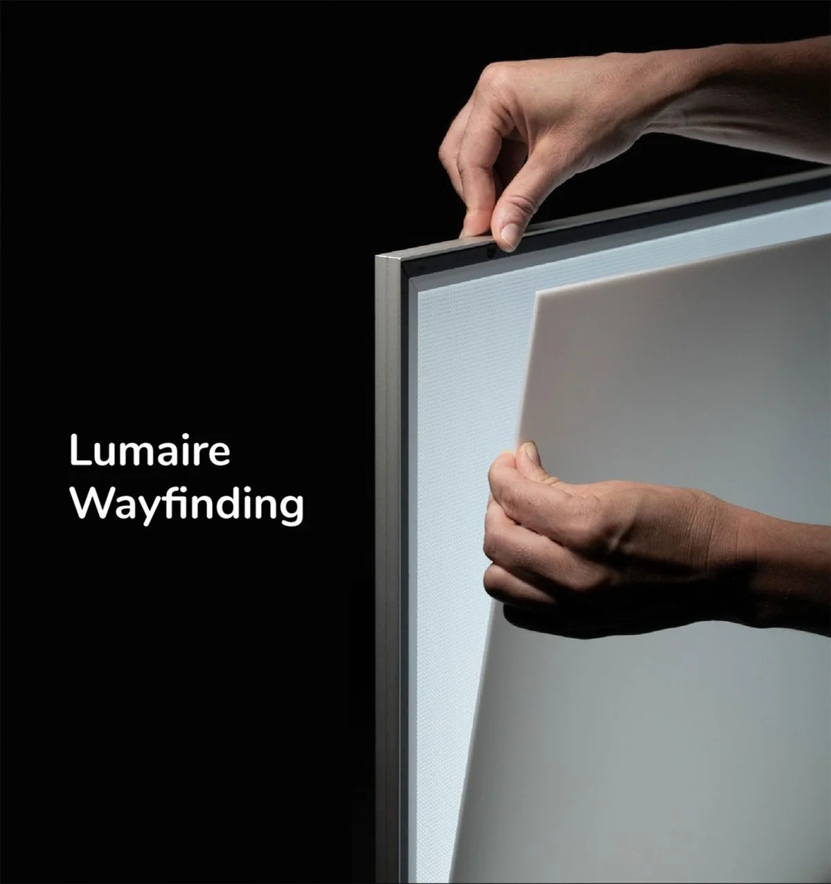 Kuva käsistä, jotka asettavat LED-näytön kehykseen, ja teksti "Lumaire Wayfinding" vasemmassa reunassa