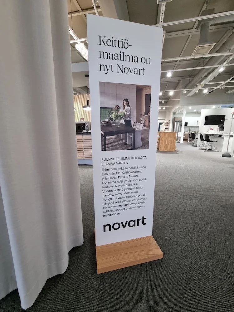 Seisova kyltti, jossa tekstiä suomeksi ja kuva keittiössä, kerrotaan Novarista ja keittiömuutoksista.