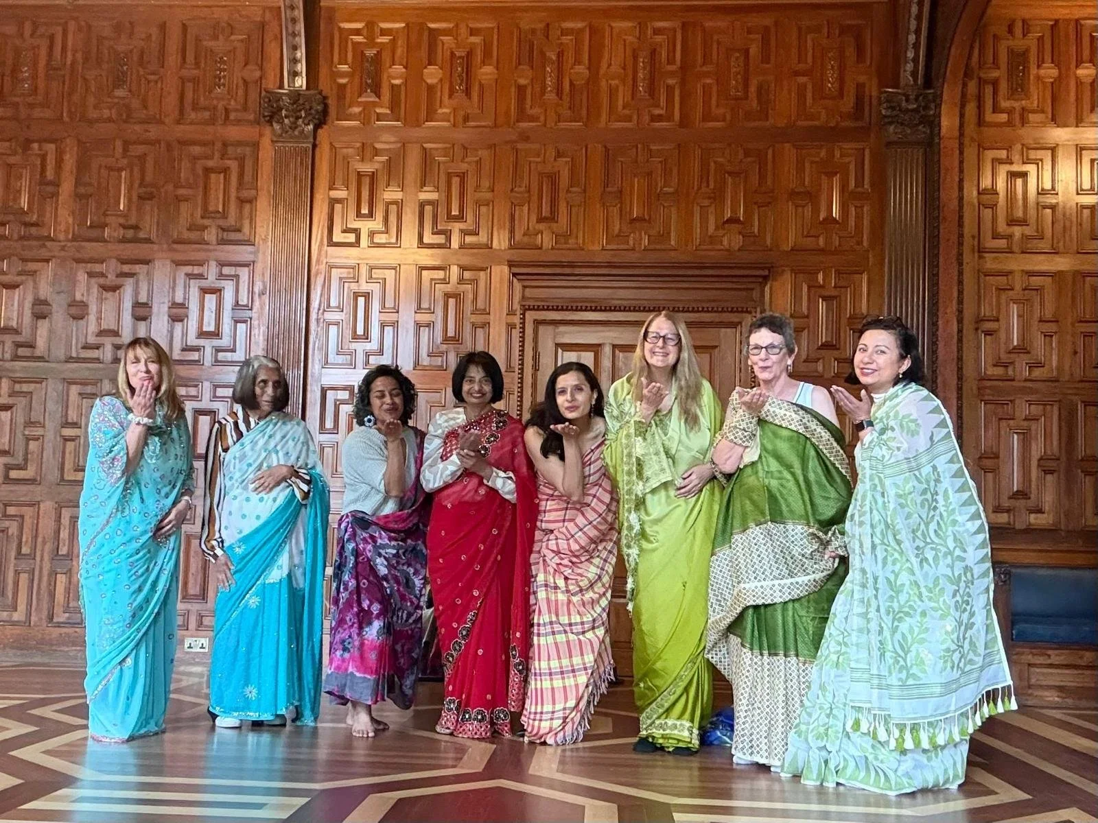 eight women draped in sarees blow kisses towards the camera