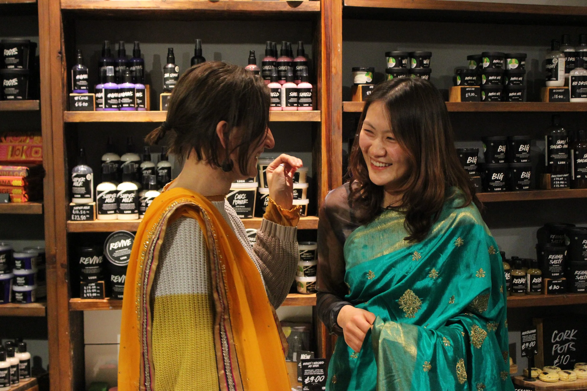 Two women wearing sarees laugh together, not looking at the camera